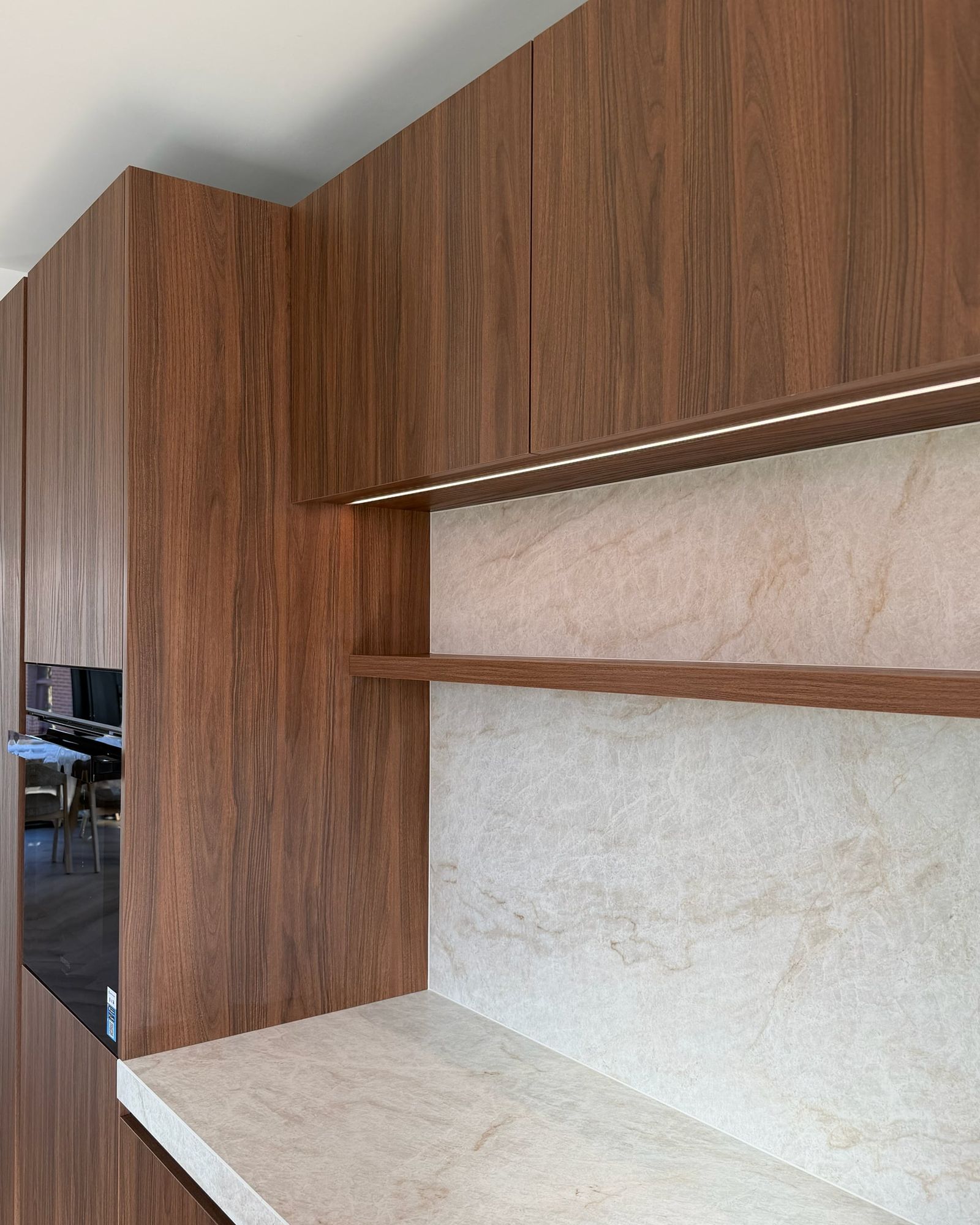 Nis in de keukenwand met stenen achterwand, zwevende walnoten plank en ledstrip onder de bovenkasten