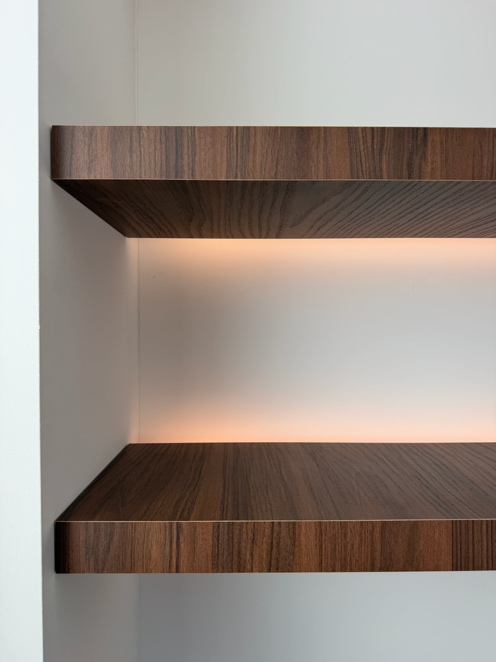 Twee zwevende walnoten planken in een witte nis met warme ledverlichting onder de bovenste plank