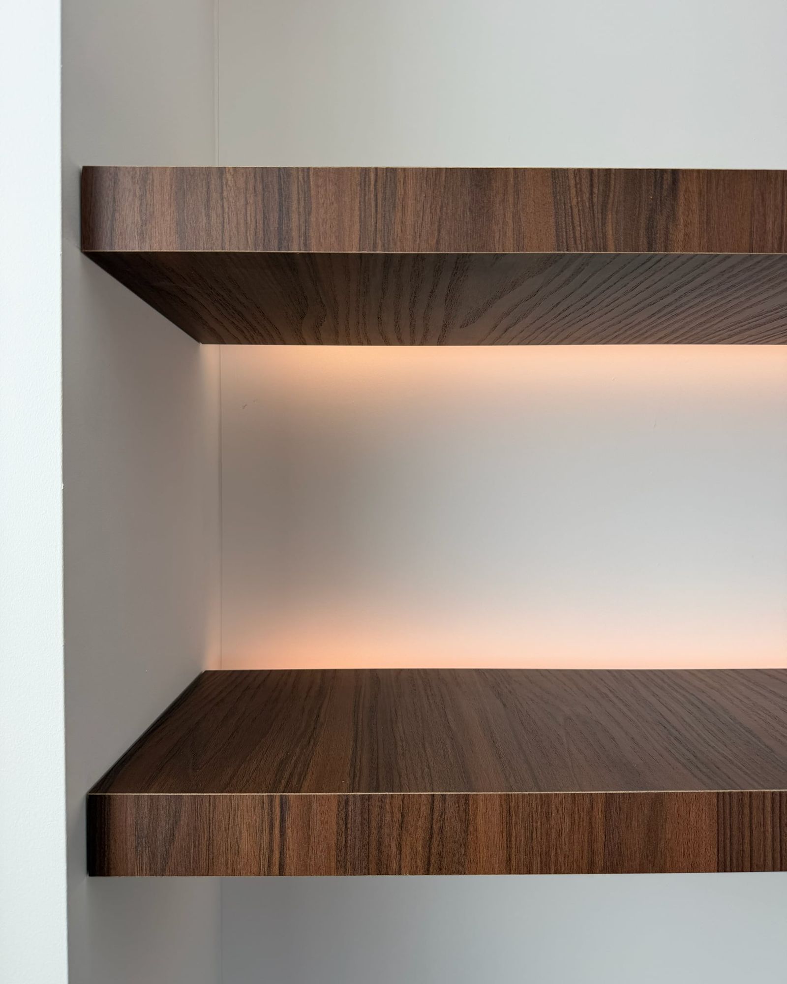 Twee zwevende walnoten planken in een witte nis met warme ledverlichting onder de bovenste plank