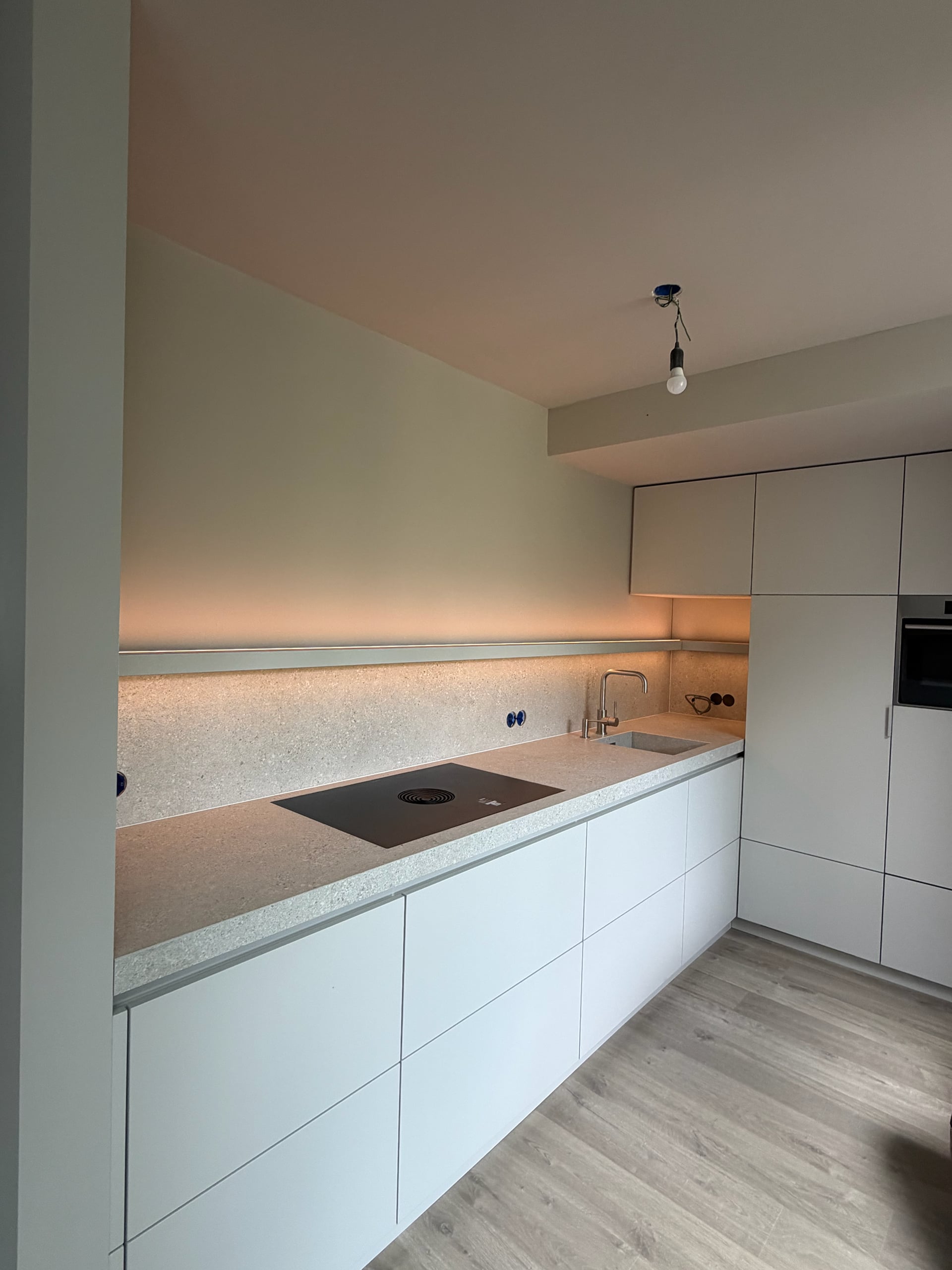 Lichtgrijze greeploze keuken met werkblad en achterwand in terrazzolook en een plank met ledverlichting