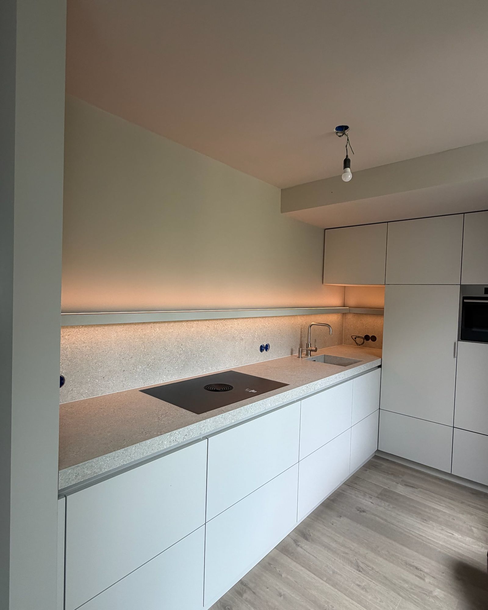 Lichtgrijze greeploze keuken met werkblad en achterwand in terrazzolook en een plank met ledverlichting