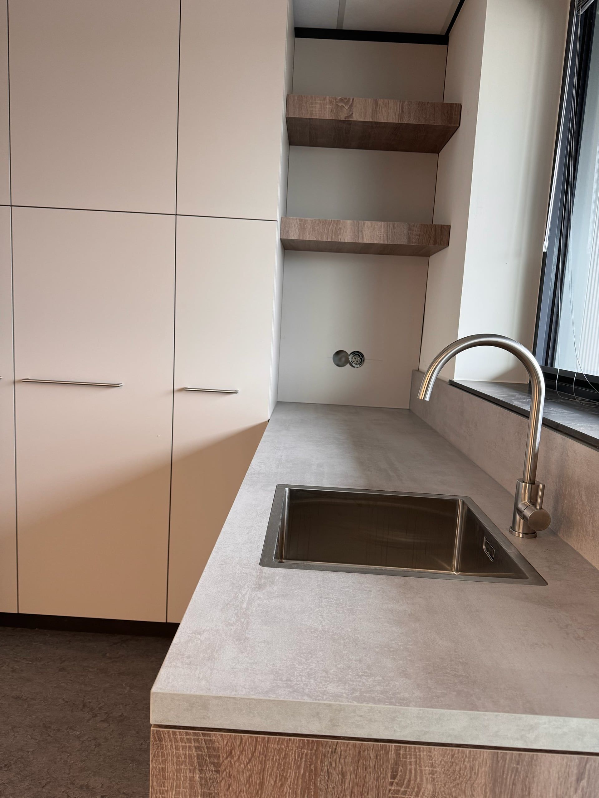 Betonlook werkblad met rvs spoelbak en kraan, naast een open nis met twee zwevende eikenkleurige planken