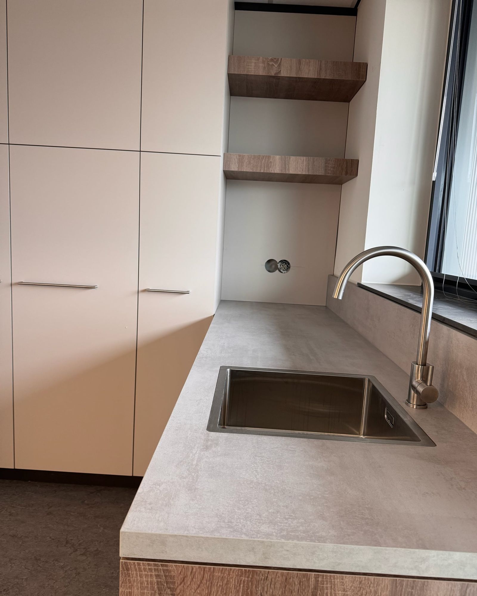 Betonlook werkblad met rvs spoelbak en kraan, naast een open nis met twee zwevende eikenkleurige planken