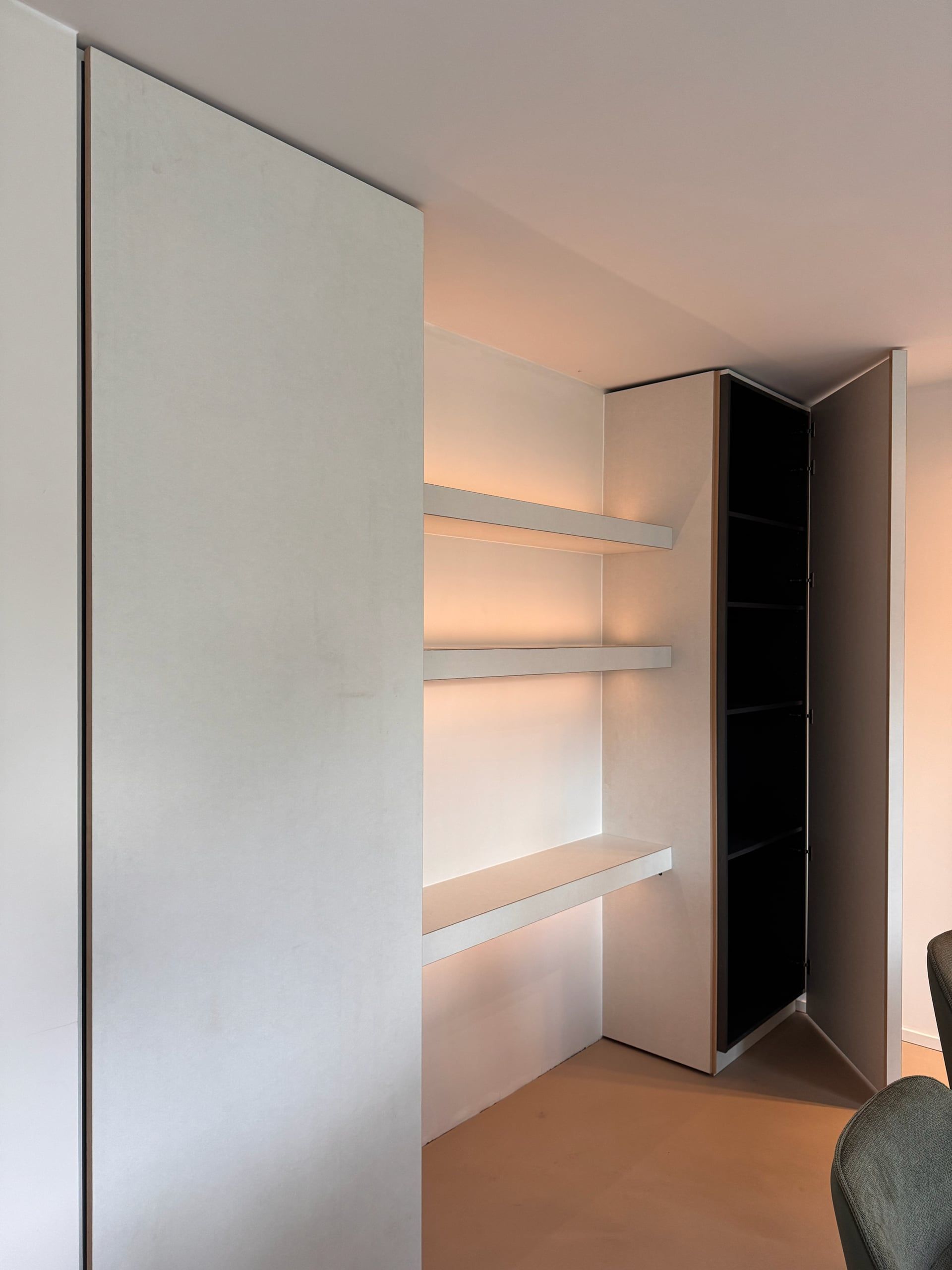 Witte kastenwand met hoge greeploze fronten, een nis met verlichte zwevende planken en een open kolomkast met zwart binnenwerk