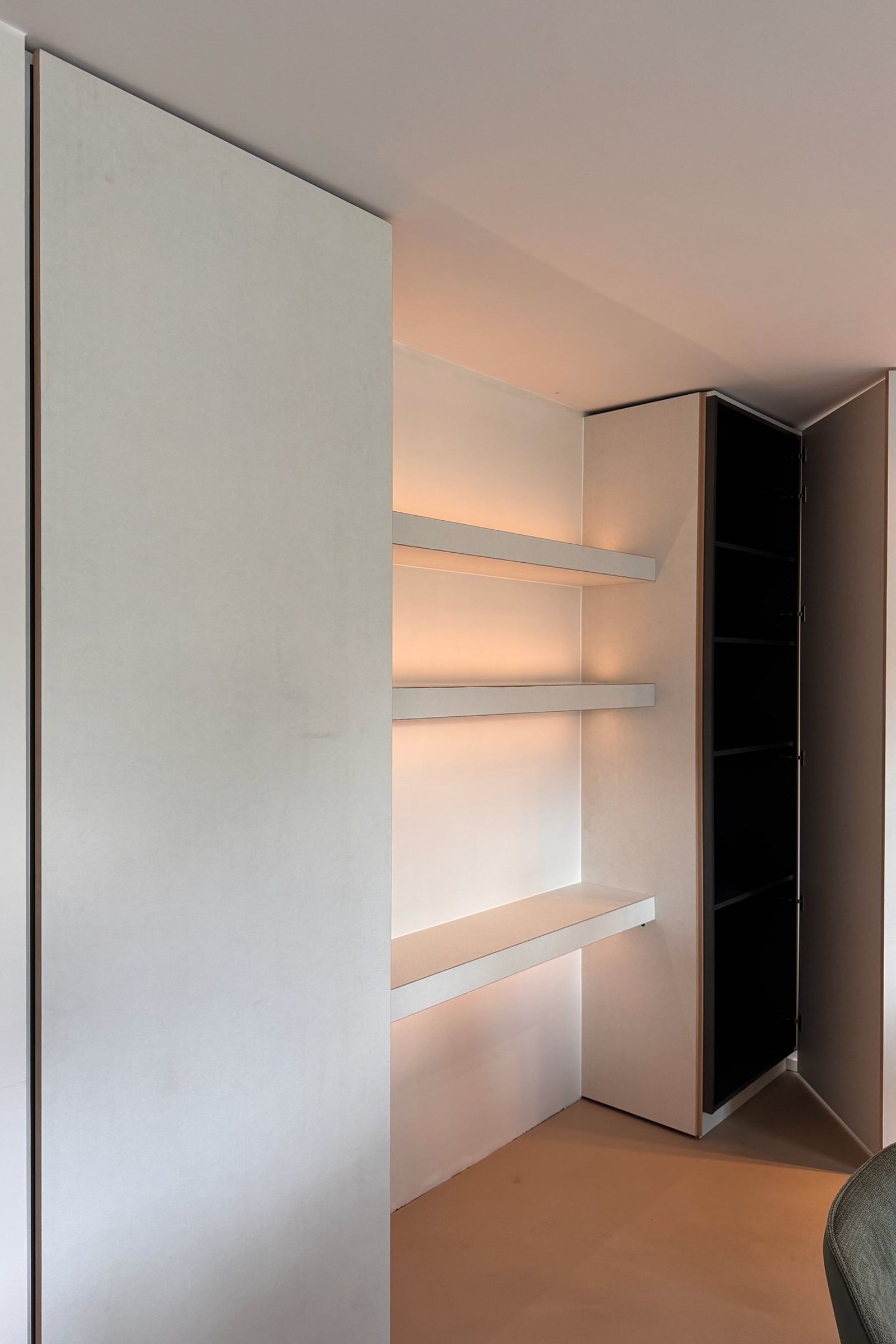 Witte kastenwand met hoge greeploze fronten, een nis met verlichte zwevende planken en een open kolomkast met zwart binnenwerk