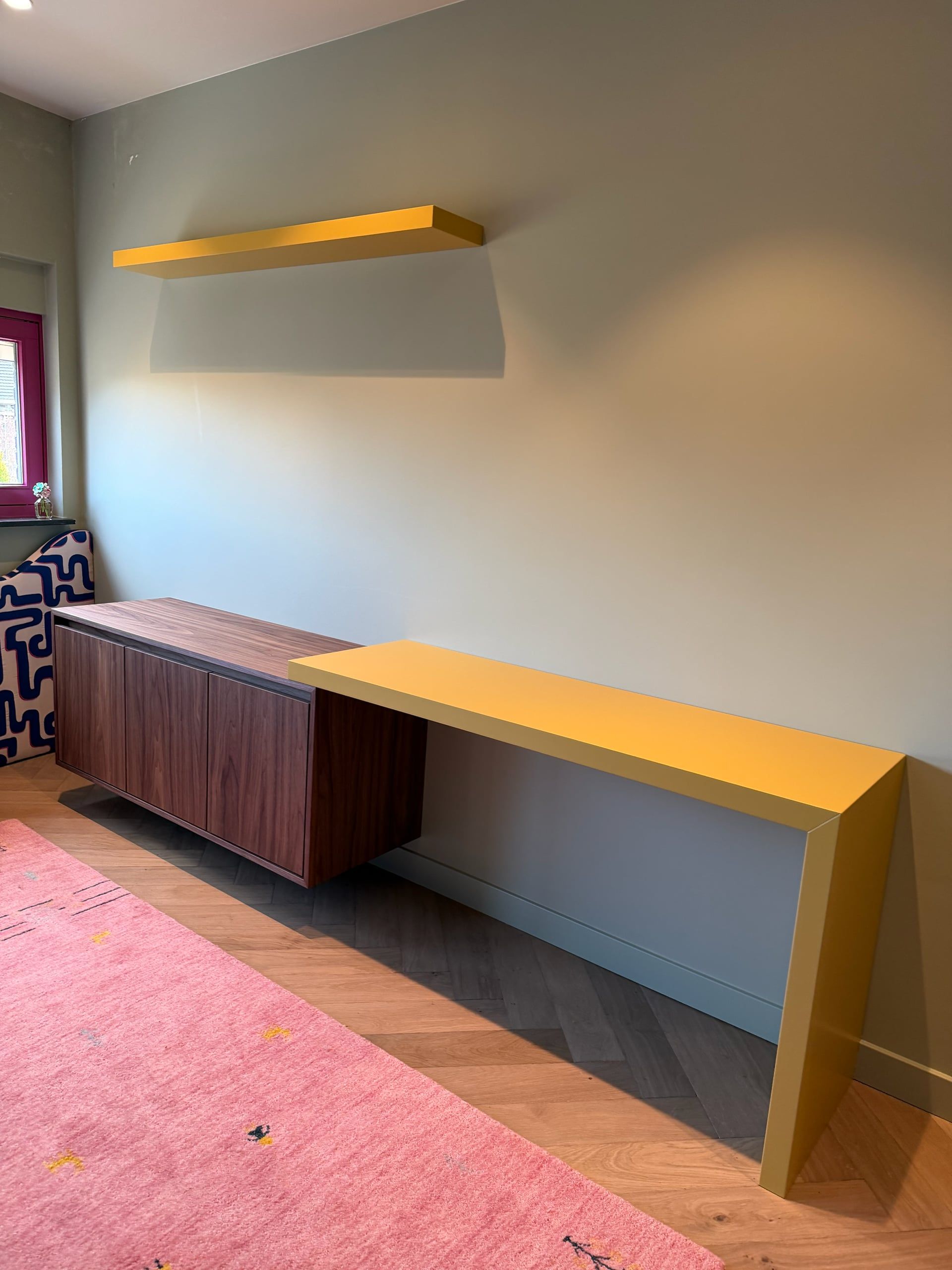 Zwevend dressoir in walnoot met een geel bureau en gele wandplank tegen een saliegroene wand