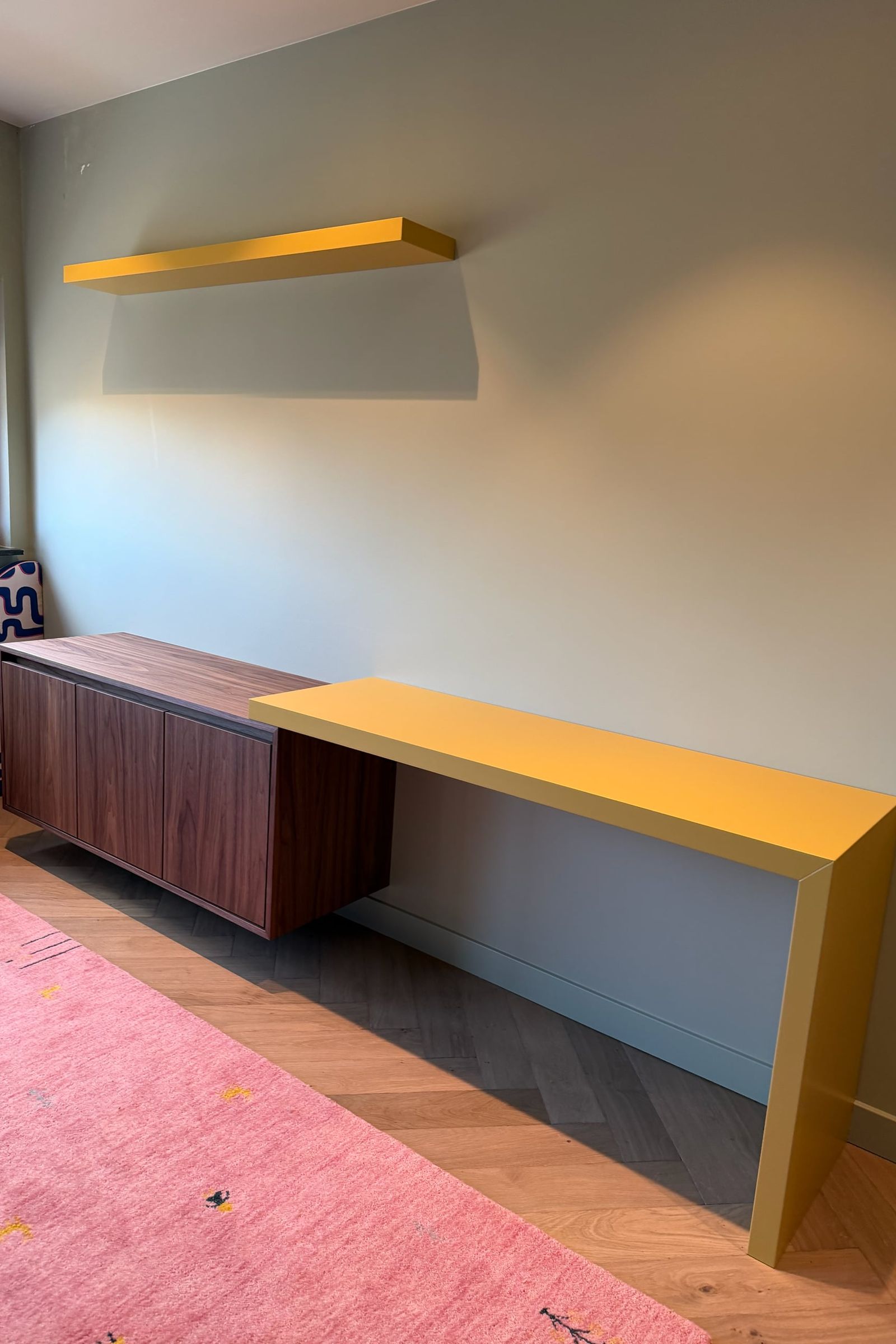 Zwevend dressoir in walnoot met een geel bureau en gele wandplank tegen een saliegroene wand