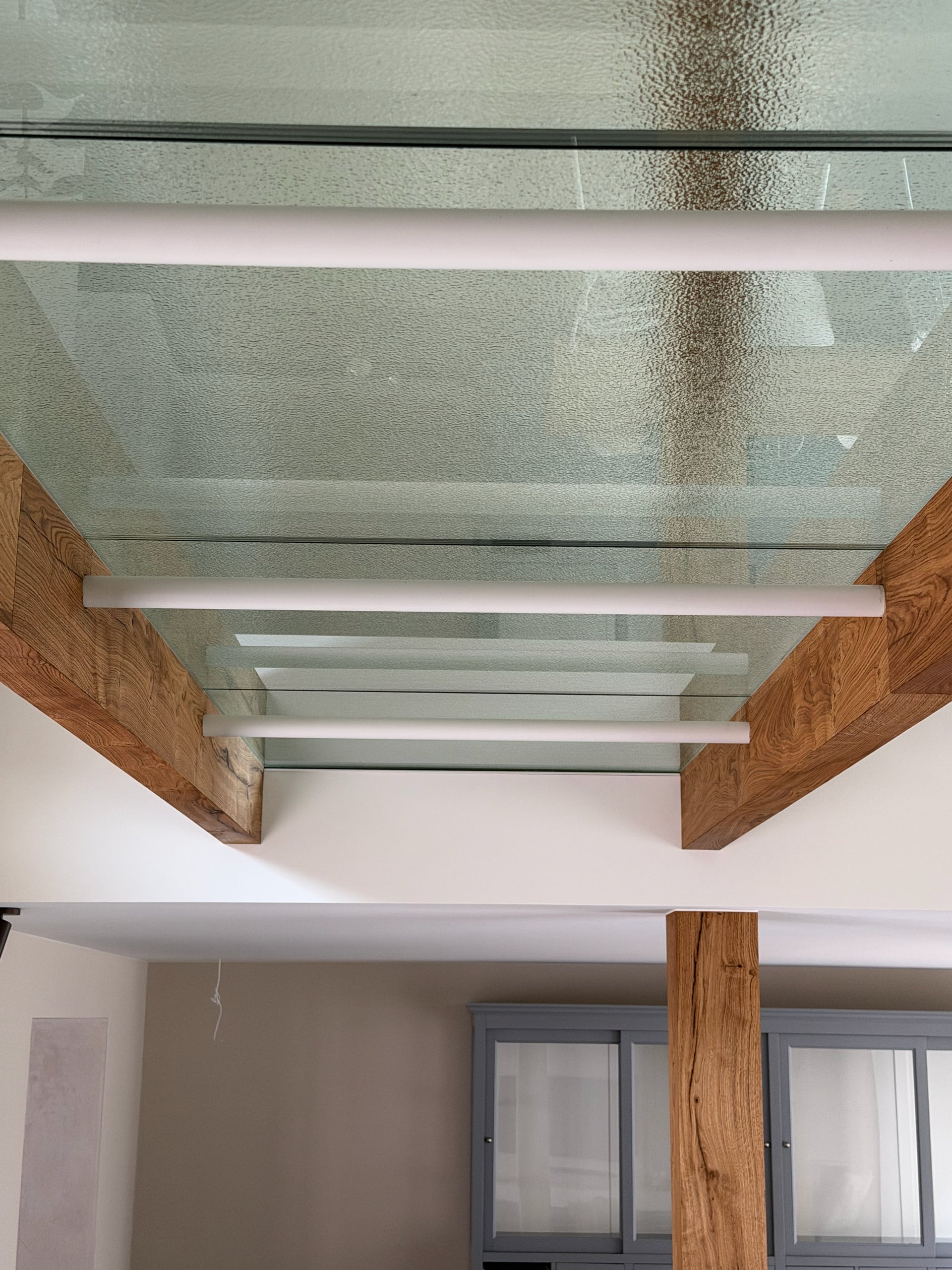 Platen structuurglas op witte buizen tussen twee eiken balken, van onderaf gezien
