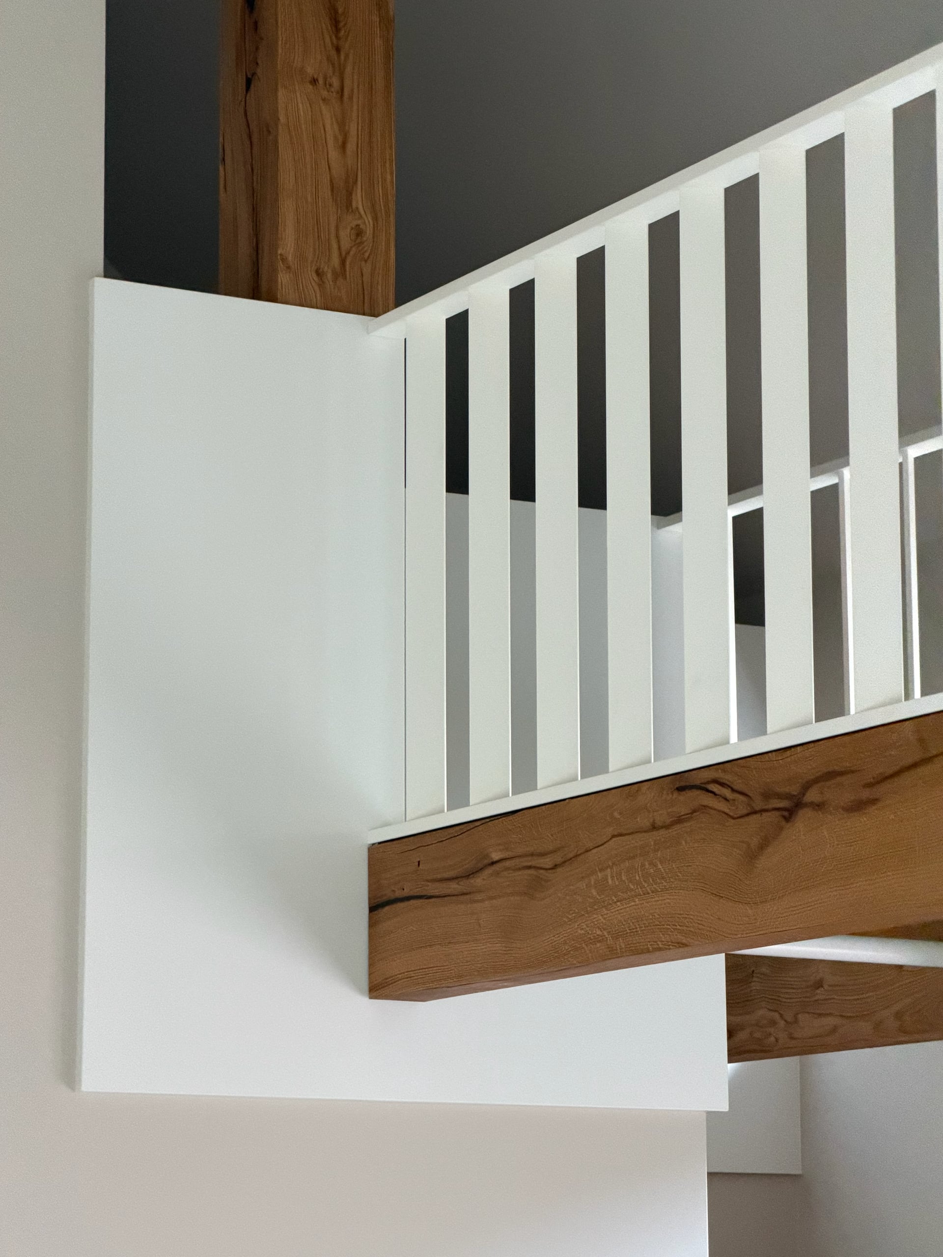 Hoek van de witte spijlenbalustrade op een eiken balk, met een eiken staander tegen een donkergrijze wand