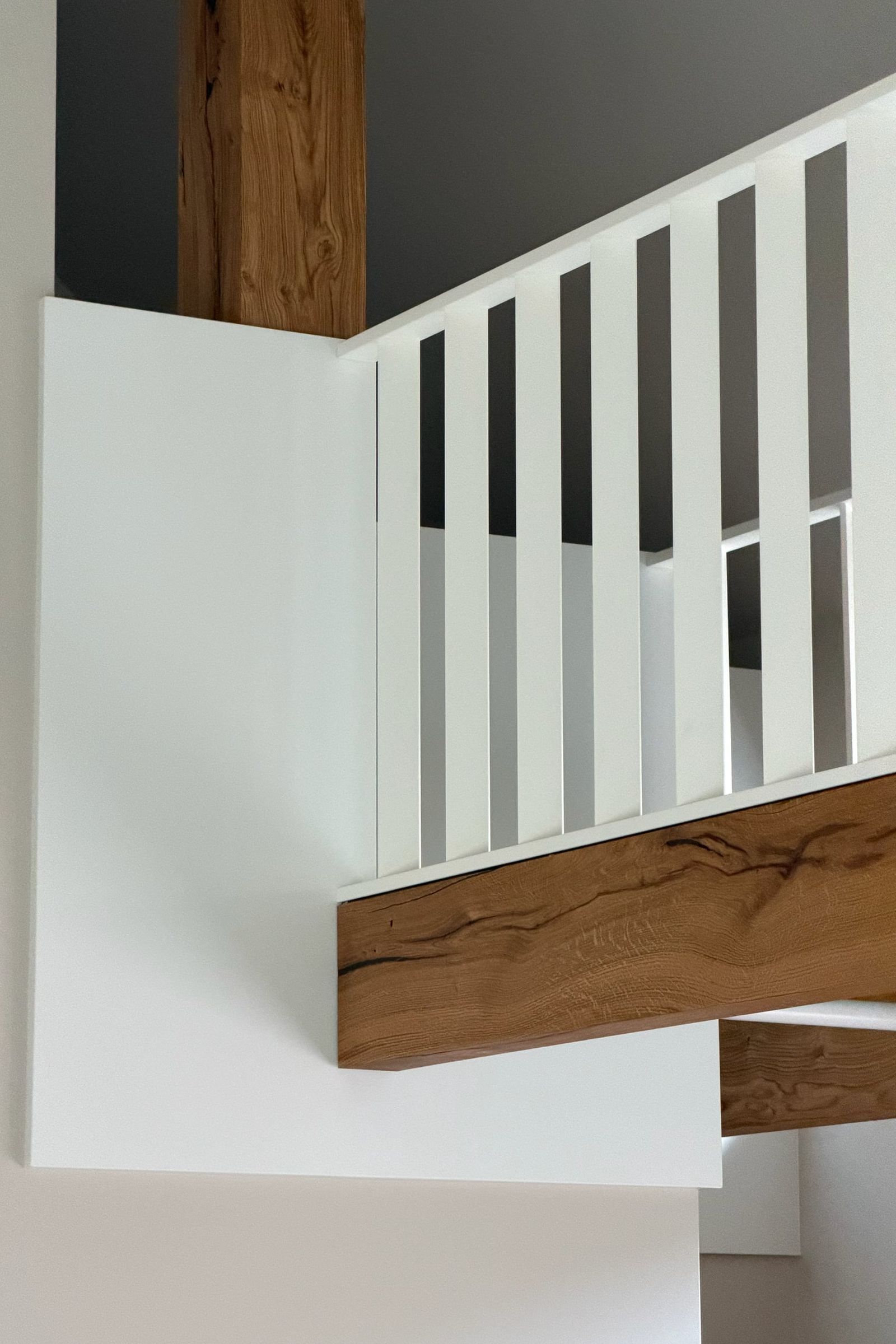 Hoek van de witte spijlenbalustrade op een eiken balk, met een eiken staander tegen een donkergrijze wand
