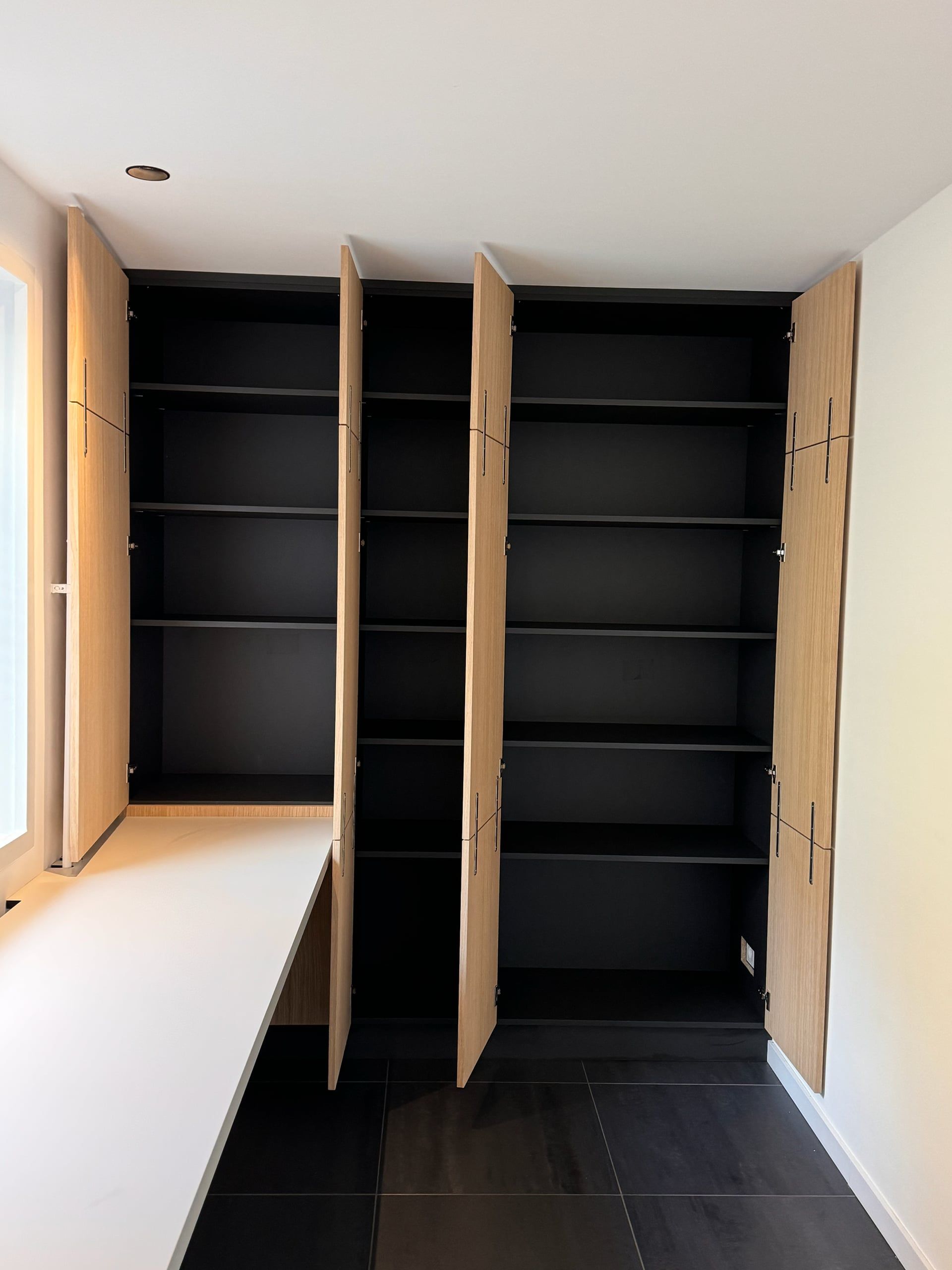 Eiken kastenwand met alle deuren open: zwart binnenwerk met legplanken over de hele hoogte, naast een wit bureaublad