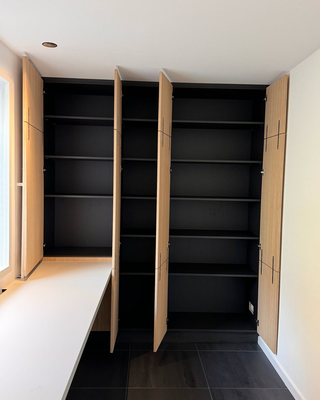 Eiken kastenwand met alle deuren open: zwart binnenwerk met legplanken over de hele hoogte, naast een wit bureaublad