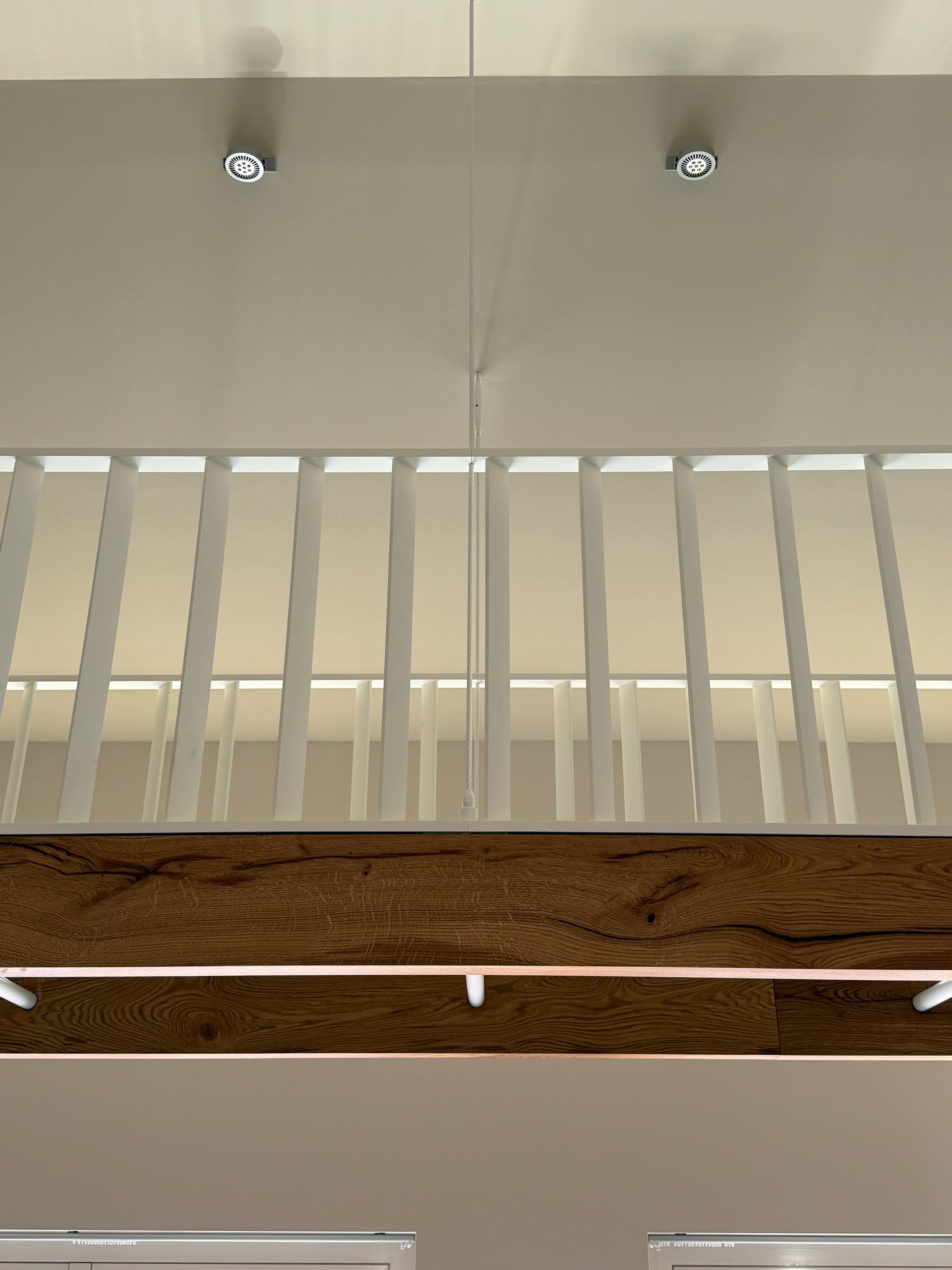 Witte spijlenbalustrade en eiken balk van onderaf gezien, met twee spots in het plafond erboven