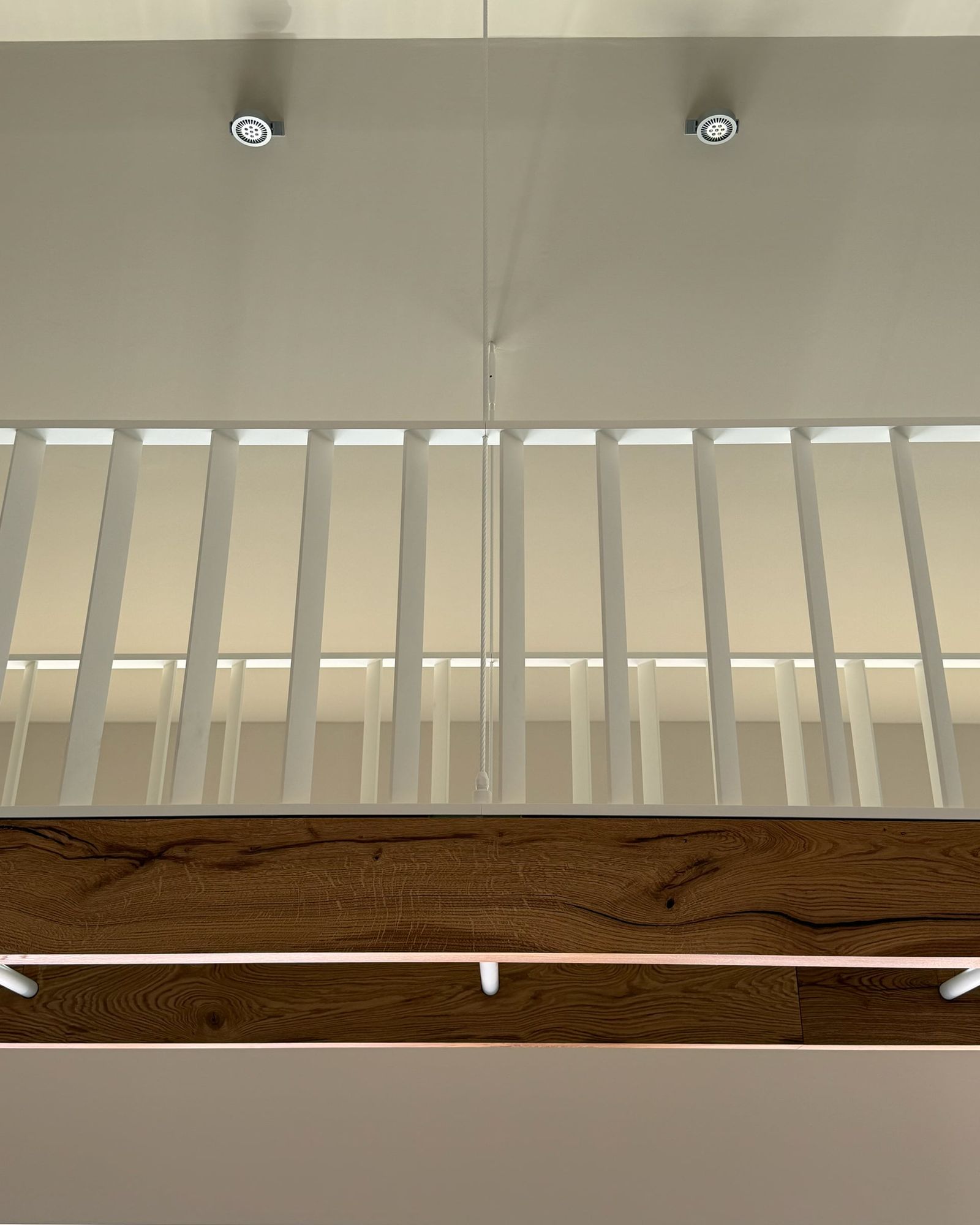 Witte spijlenbalustrade en eiken balk van onderaf gezien, met twee spots in het plafond erboven