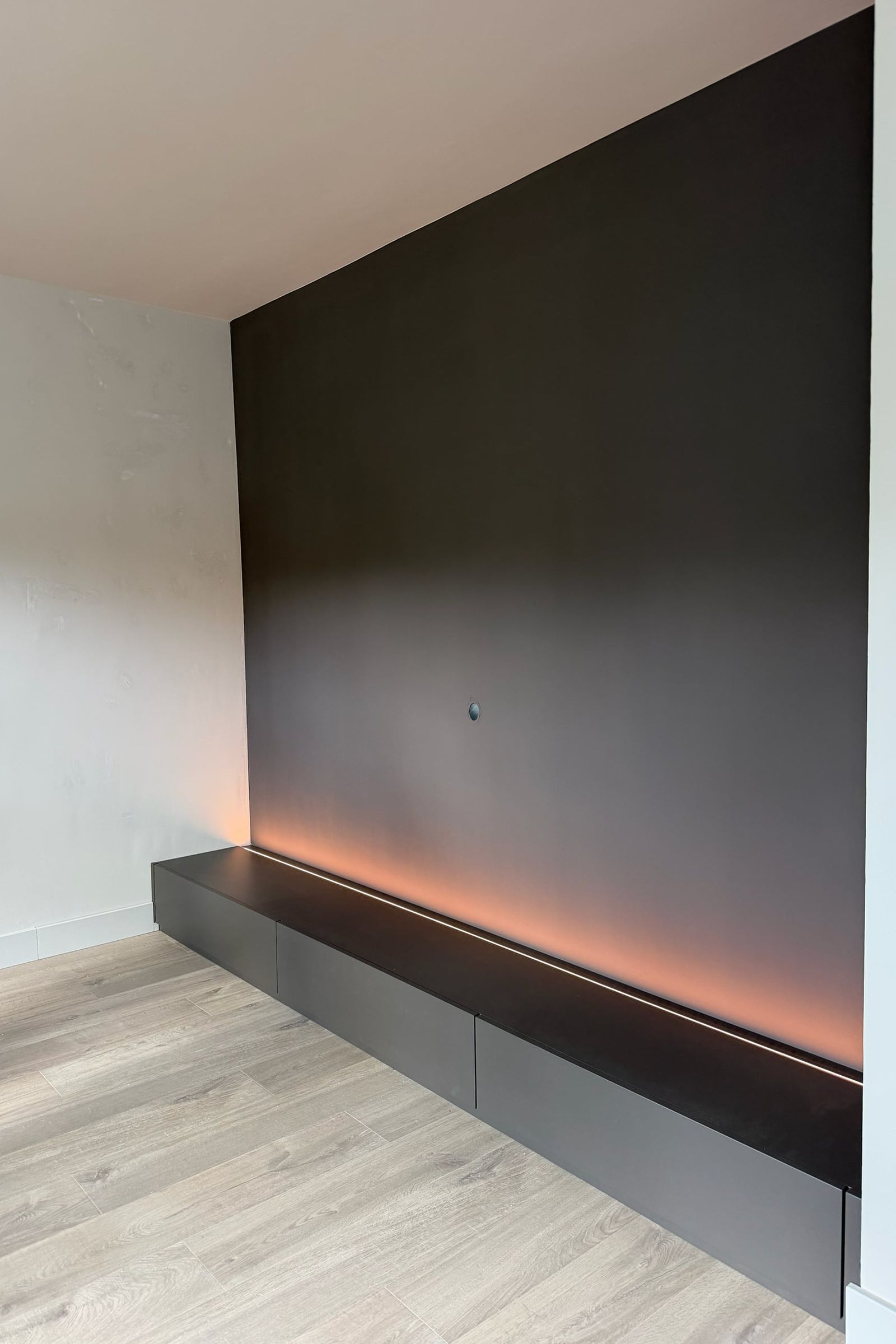 Laag antracietkleurig tv-meubel met laden over de volle breedte van een donkere wand, met ledstrip erachter