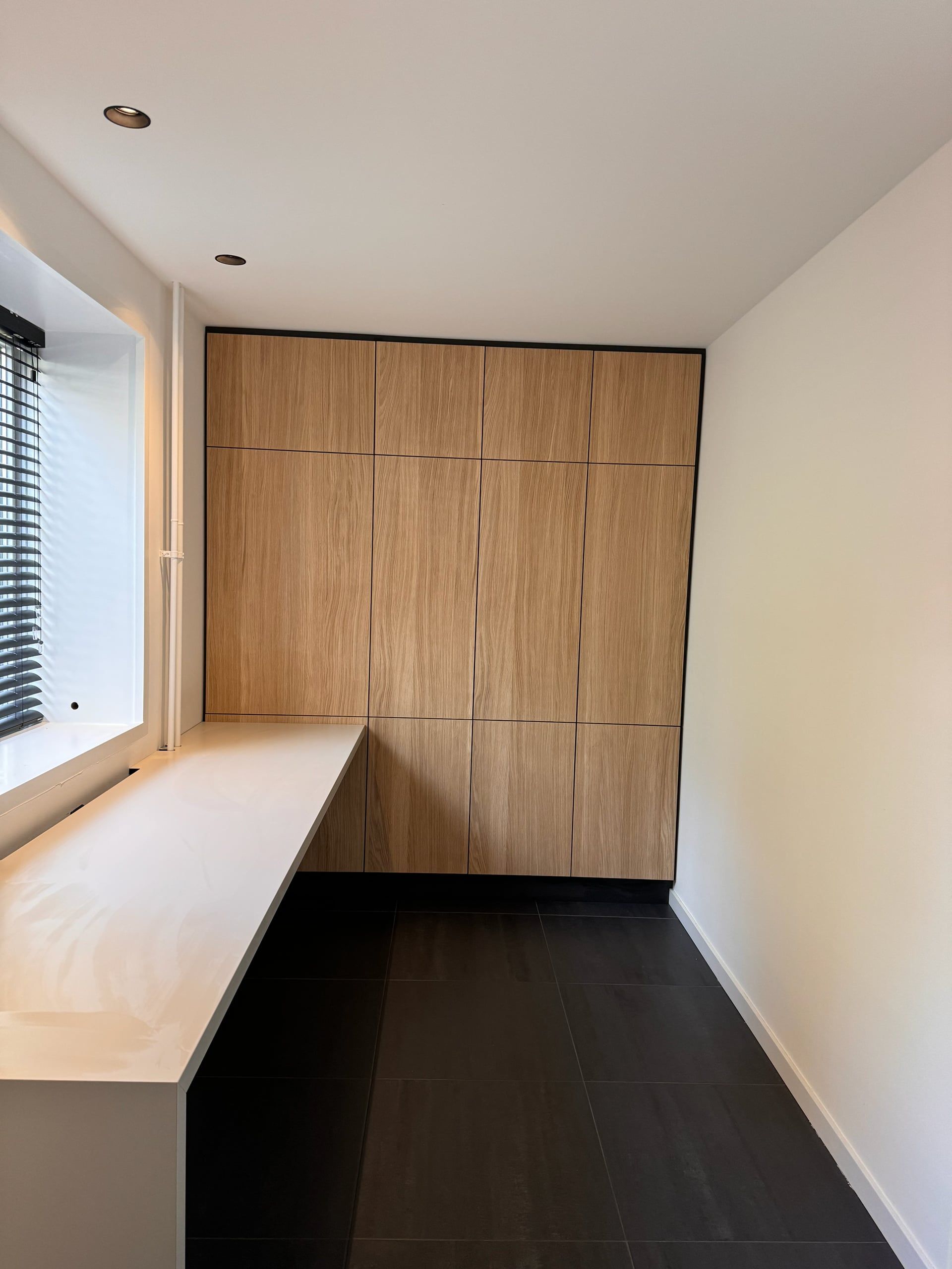 Werkkamer met een eiken kastenwand tot het plafond, greeploze fronten en een lang wit bureaublad langs het raam