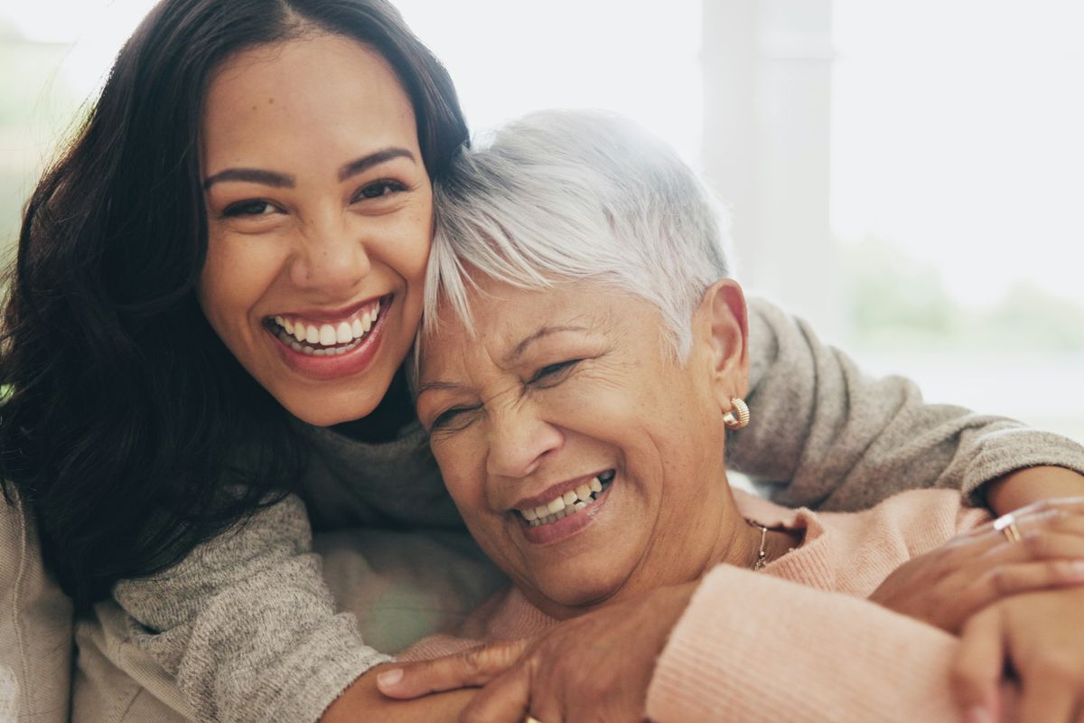 A younger and older woman embracing and laughing together at home