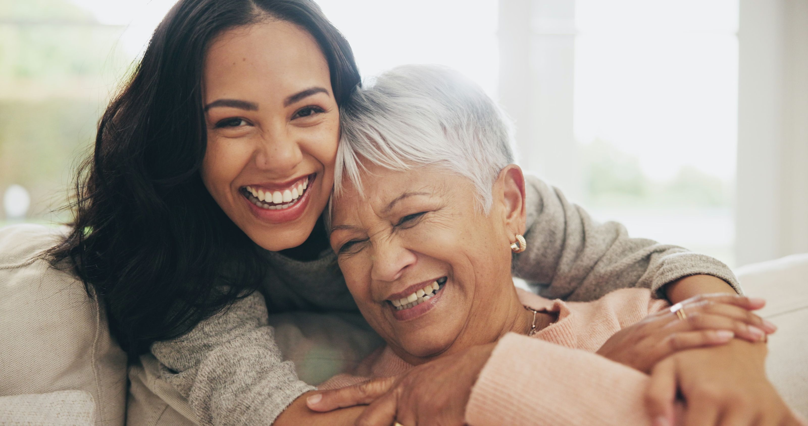 A younger and older woman embracing and laughing together at home