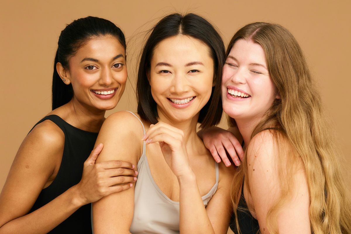 Three women standing close together and smiling in warm natural light