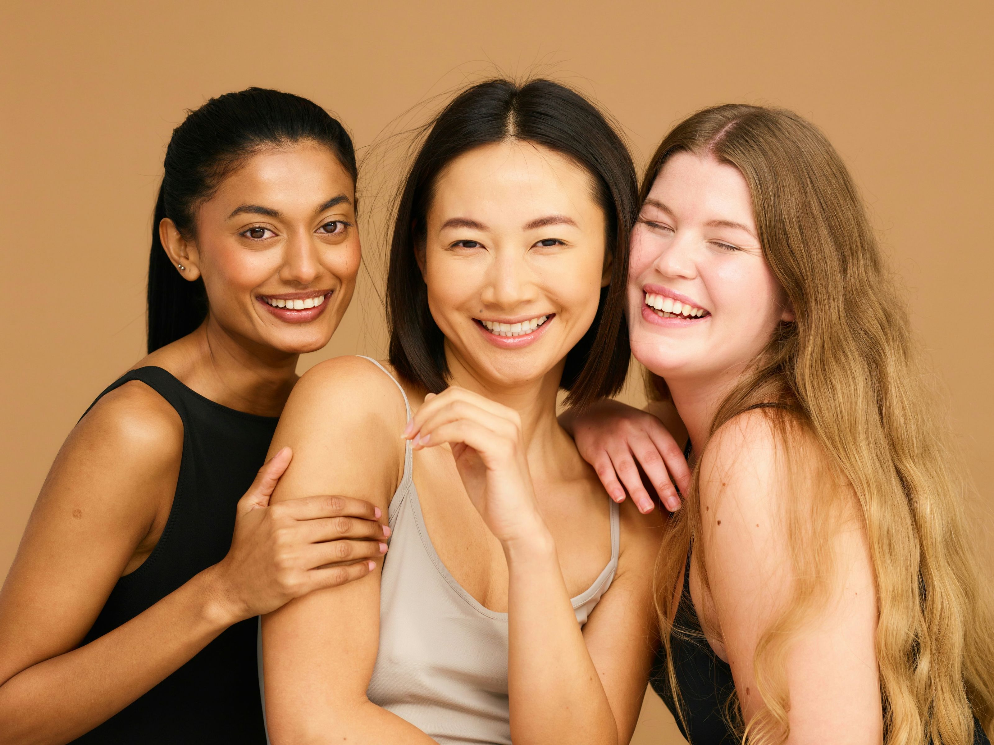 Three women standing close together and smiling in warm natural light