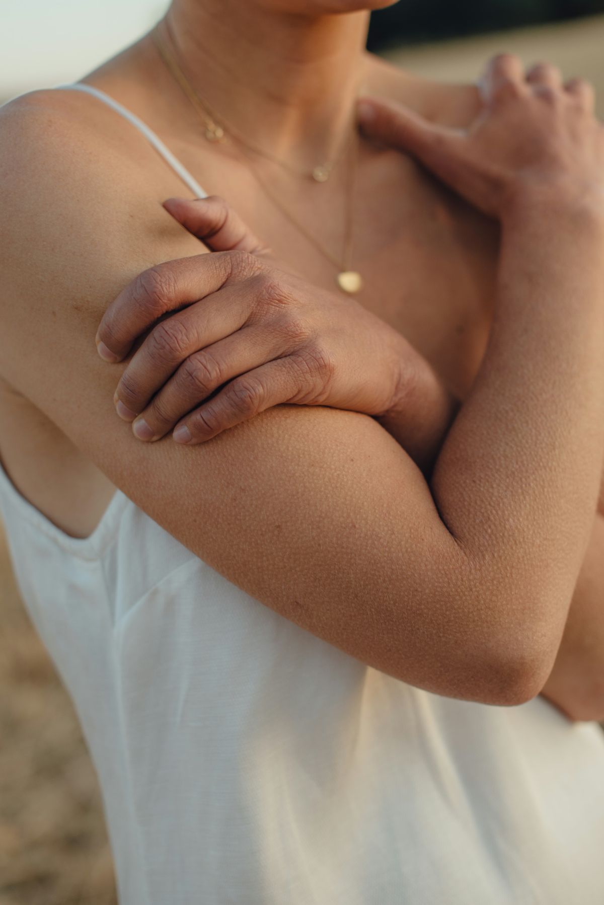 A woman with her arms folded gently across her chest in warm evening light