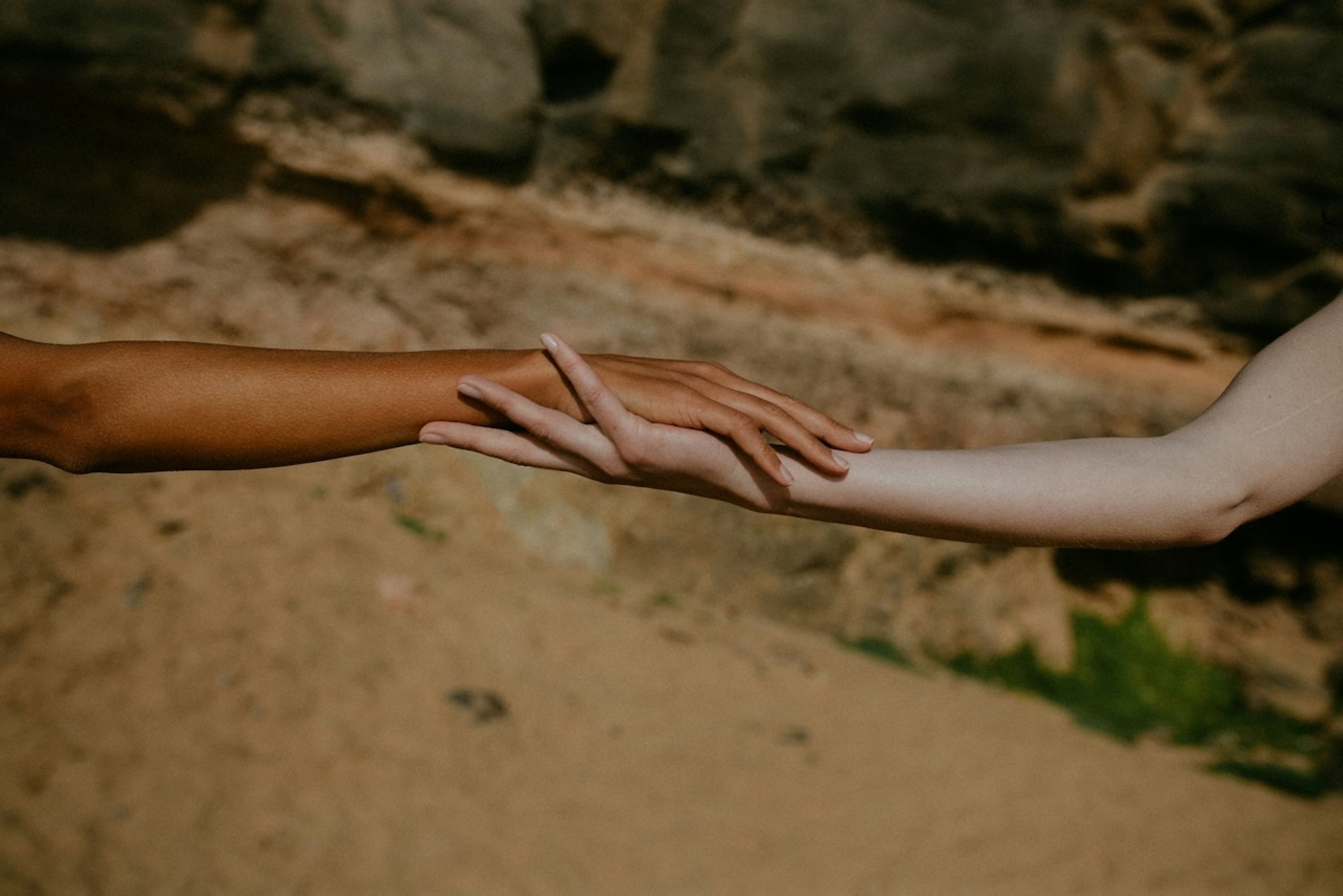 Two people reaching toward each other, fingertips nearly touching, in warm light
