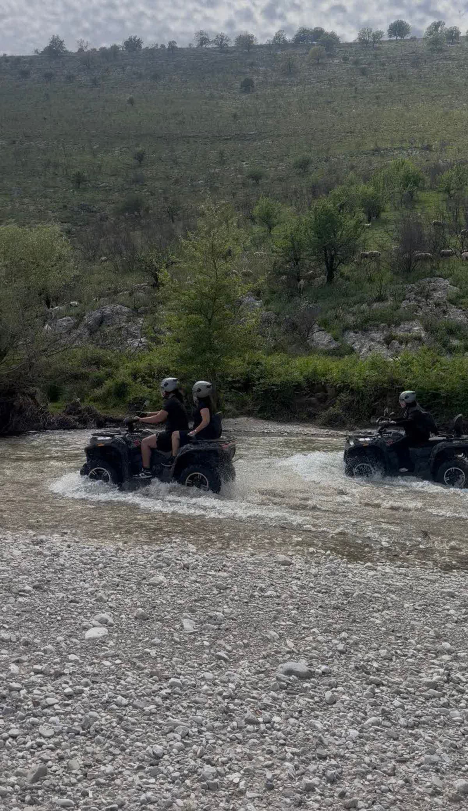 Riders crossing a river through green spring hills near Saranda
