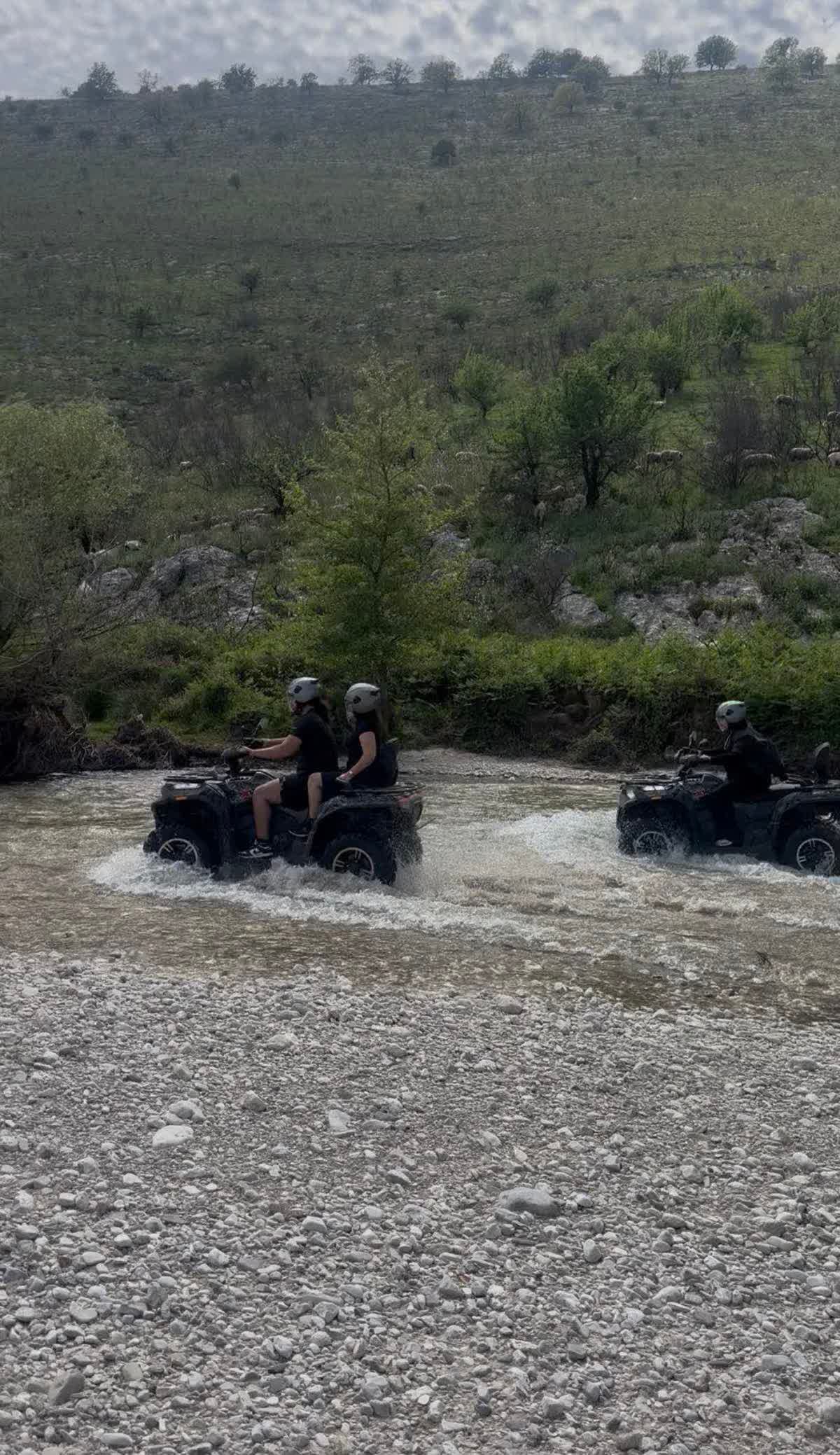 Riders crossing a river through green spring hills near Saranda