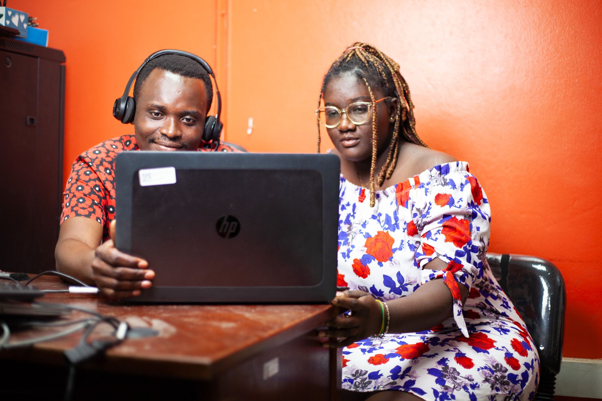 A male employee with a headset and a female colleague quietly observing a laptop screen.