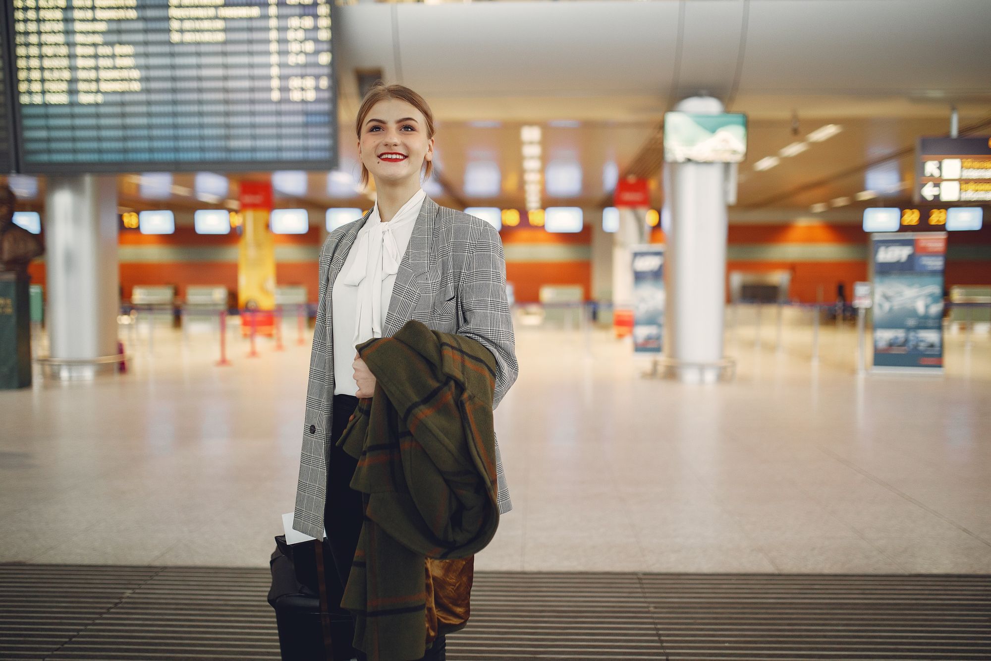A traveller with luggage standing by an airport departure board