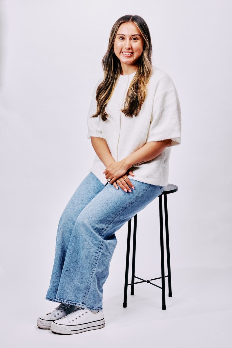 Studio portrait of a woman seated on a stool against a white backdrop