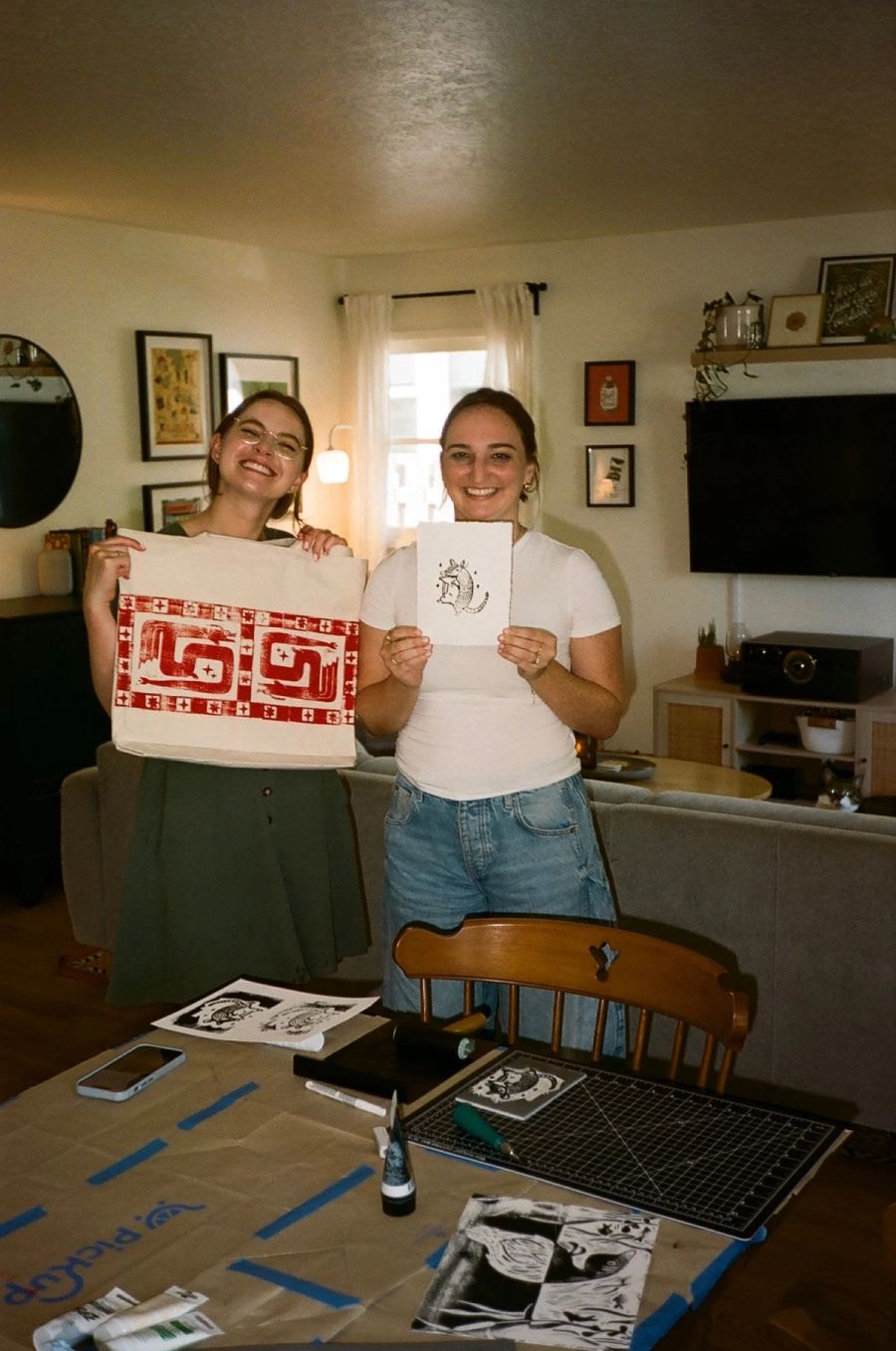 Two Sproutbox teammates showing off a block-printed tote bag and an armadillo print at a printmaking session