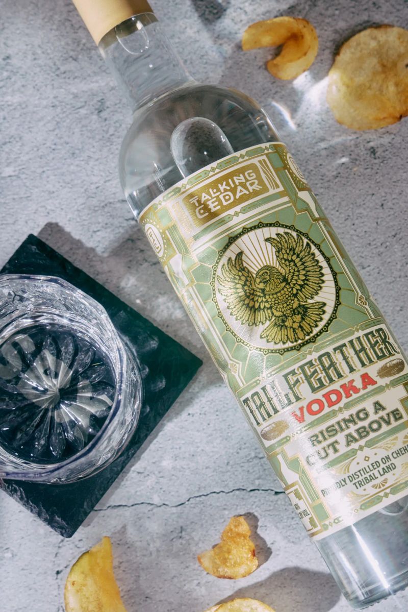 Overhead shot of a Tailfeather Vodka bottle, rocks glass, and chips on a concrete surface