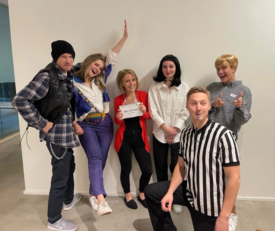 Sproutbox team in Halloween costumes posing against a white wall, one holding a No Costume Costume sign