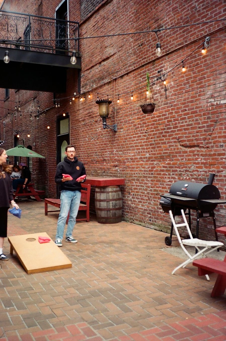 Sproutbox teammate playing cornhole in a brick courtyard strung with lights