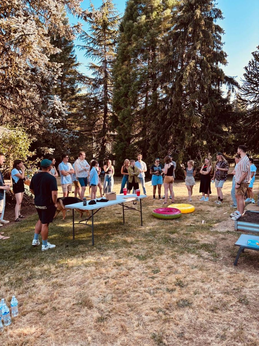 Sproutbox team standing in a circle in a backyard under tall evergreen trees at a summer party