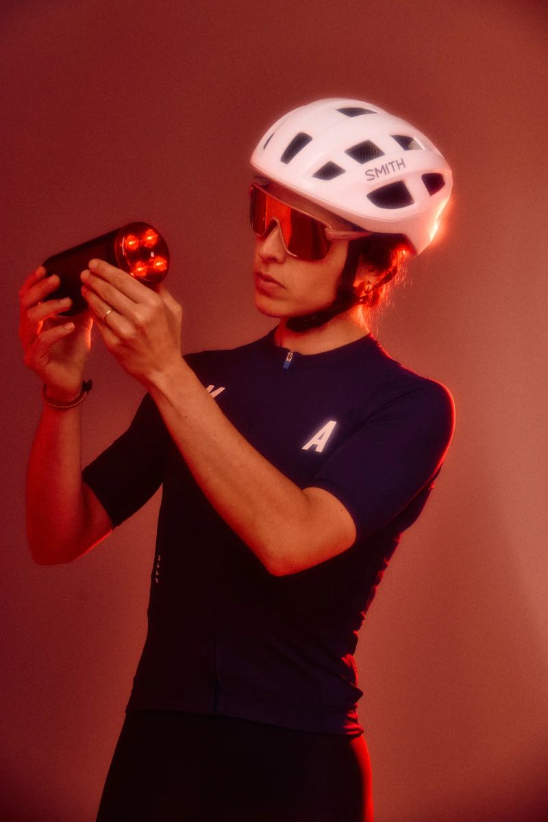 Cyclist in a helmet and sport sunglasses inspecting a red bike light under moody red lighting