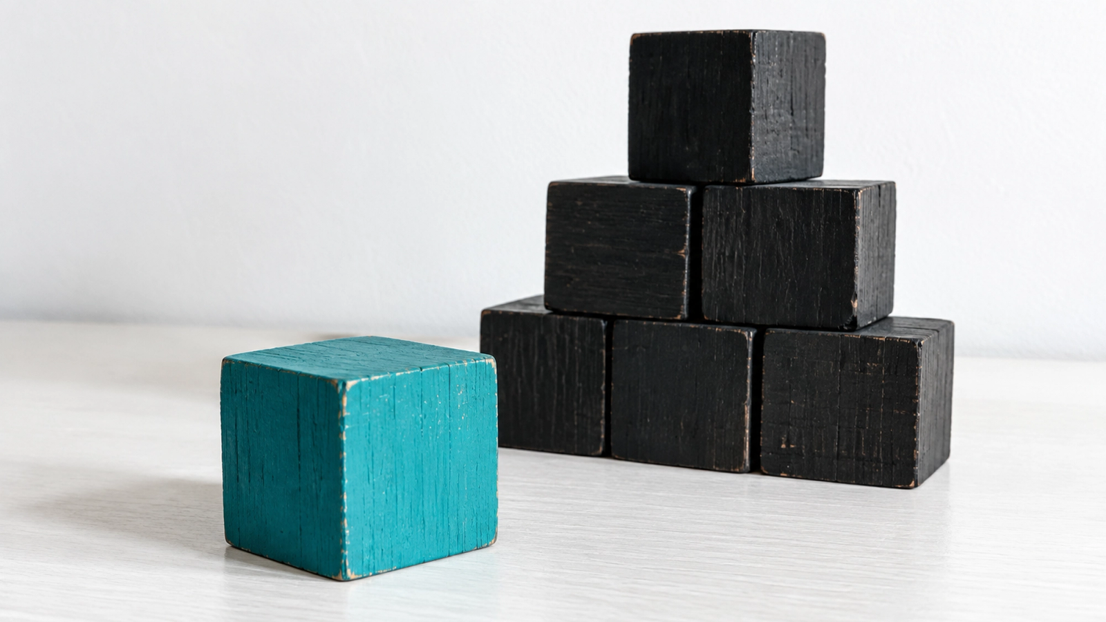 The concept goes first. The details stack behind it. One turquoise block placed before a stack of black blocks, illustrating concept-before-detail in AI explainer content