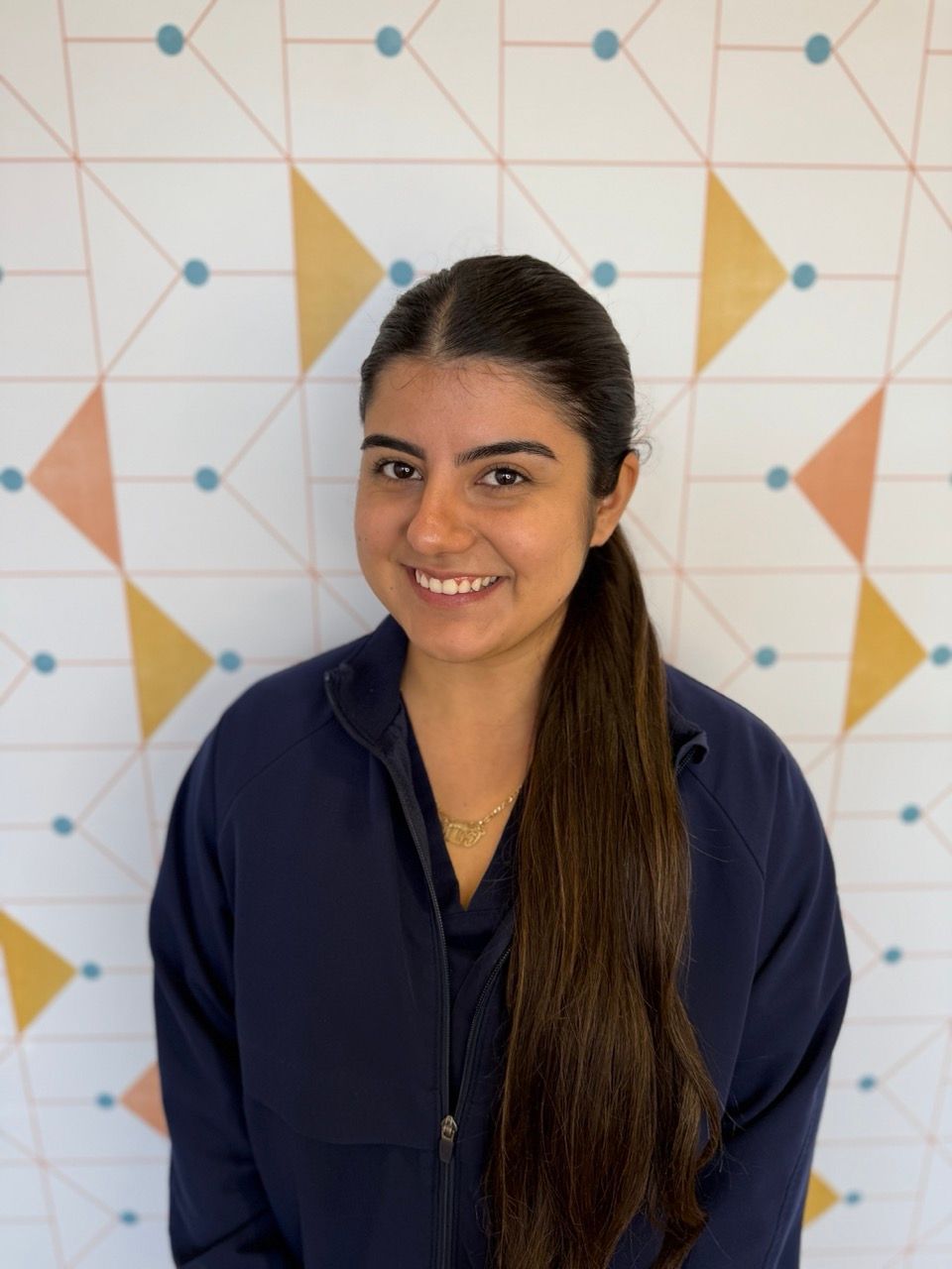 Poppy Kids dental assistant Alexandra stands leaning against a patterned wall.