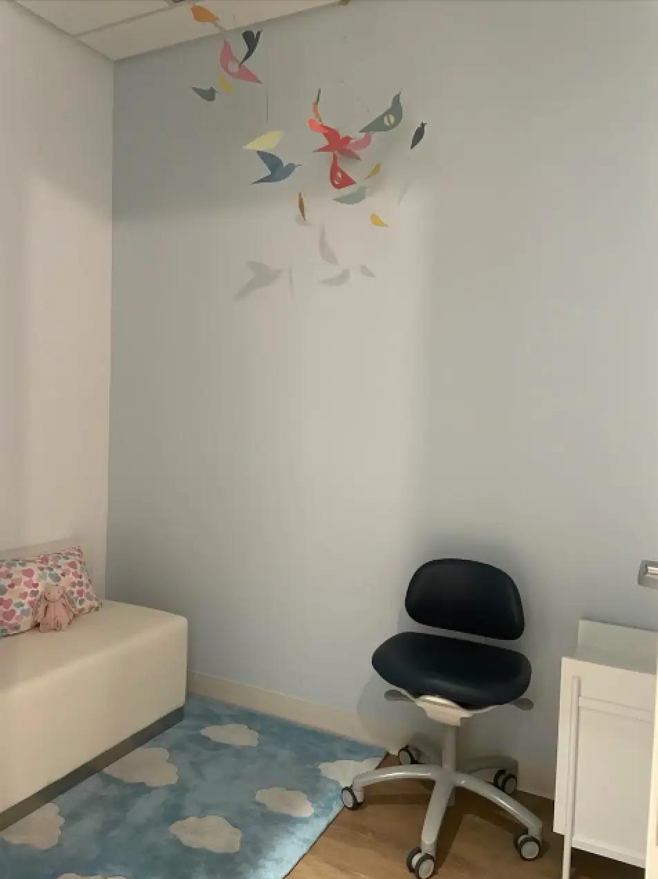 A cozy infants treatment area in a dental office with a white bench, a colorful cushion, and a blue cloud-patterned rug on the floor.