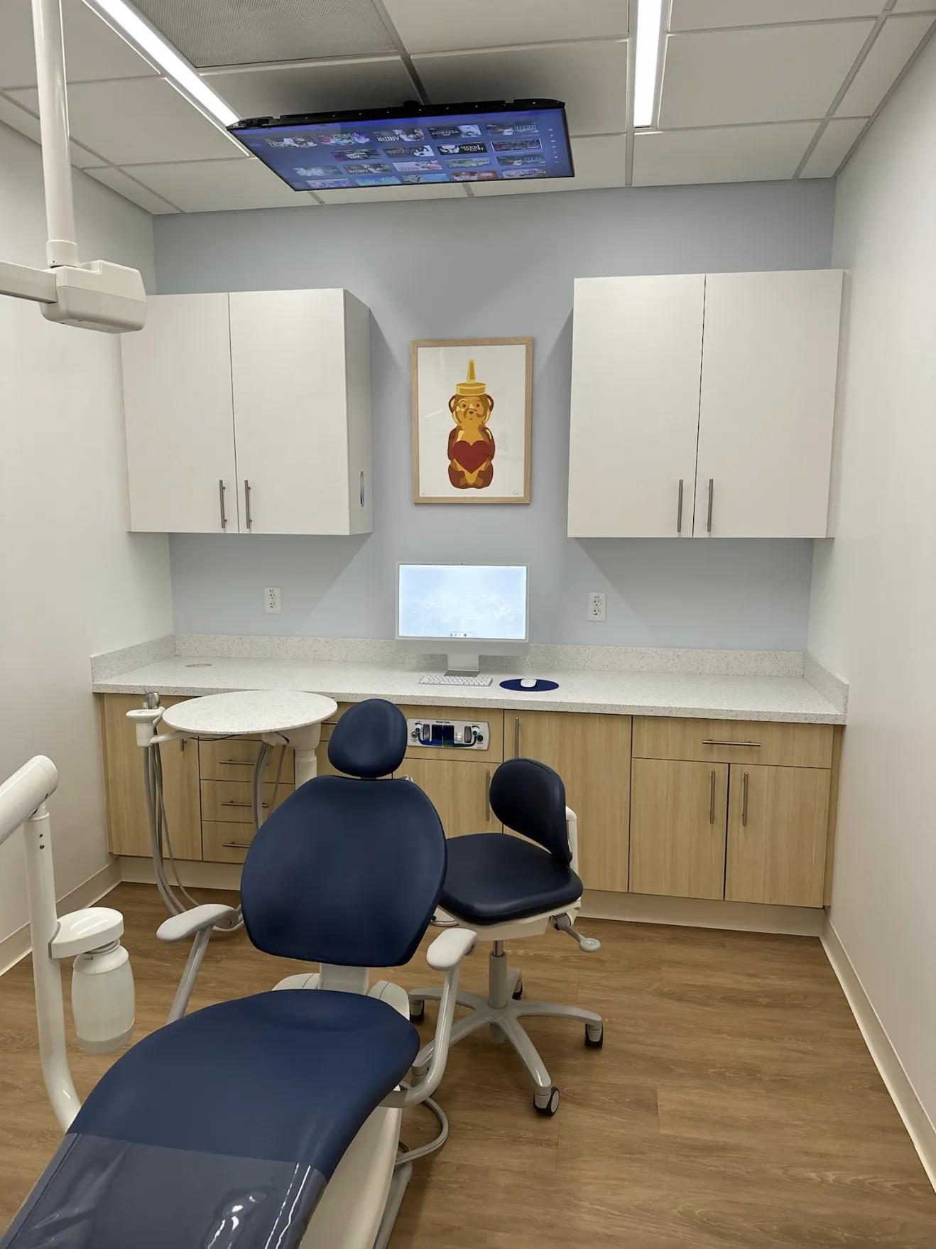 Poppy Kids Dental Operation room with a blue dental chair, wooden cabinets, a computer monitor, and a framed picture of a cartoon bear by San Francisco artist fnnch.