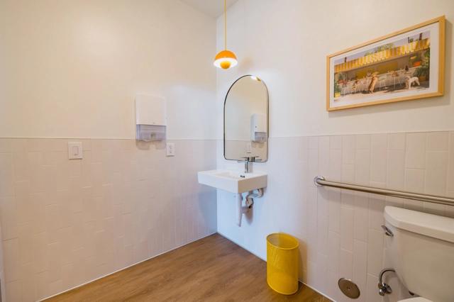A clean, modern bathroom with a white sink, a large mirror with rounded corners, and a bright orange pendant light overhead.