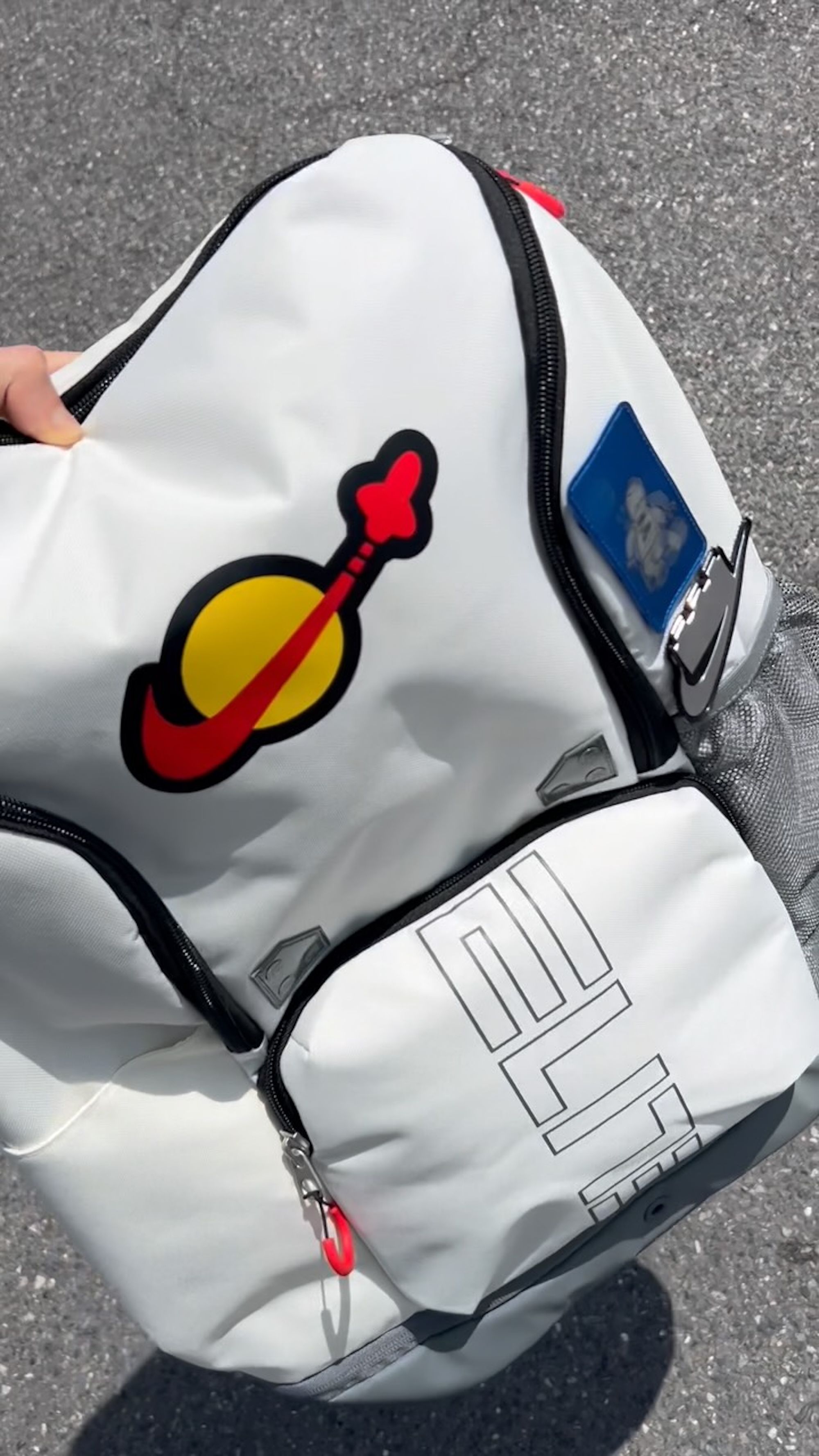 LEGO® x Nike Varsity Elite Backpack (32L) in a "Sail/Smoke Grey/Rush Red" color scheme.