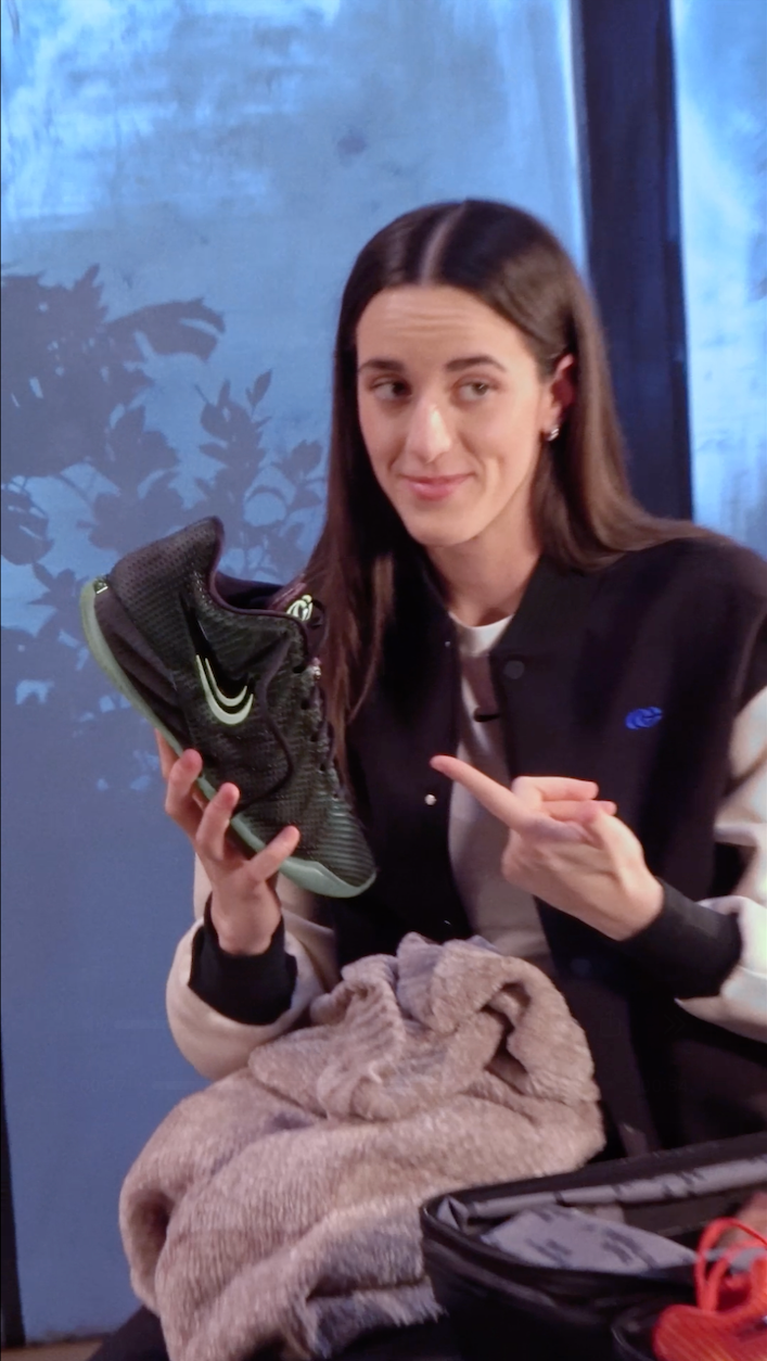 Caitlin Clark showing off Nike Caitlin 1 "Halloween" basketball shoe in a "Black/Ghost Green/Mint Foam/Racer Blue" color scheme.