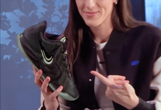 Caitlin Clark showing off Nike Caitlin 1 "Halloween" basketball shoe in a "Black/Ghost Green/Mint Foam/Racer Blue" color scheme.