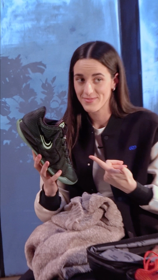 Caitlin Clark showing off Nike Caitlin 1 "Halloween" basketball shoe in a "Black/Ghost Green/Mint Foam/Racer Blue" color scheme.