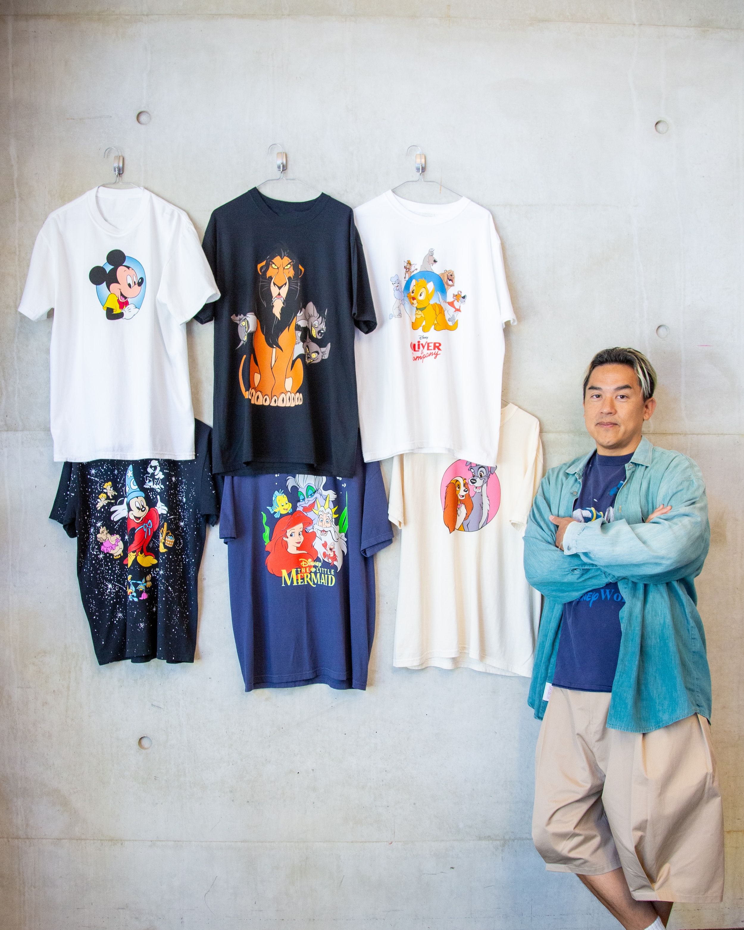 Bobby Kim, Global Creative Director, Disney Consumer Products, posing next to six graphic t-shirts from his Collection 1: Classics collaboration.