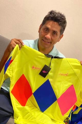Jorge Campos holding an ACA Sport Retro Jersey, featuring fluorescent diamonds across the chest and a neon yellow base.