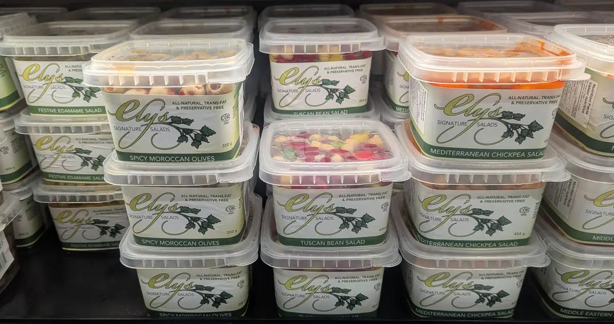 Ely's salads on a cooler shelf in the previous packaging: identical white and green wraparound labels with a parsley illustration on every flavour
