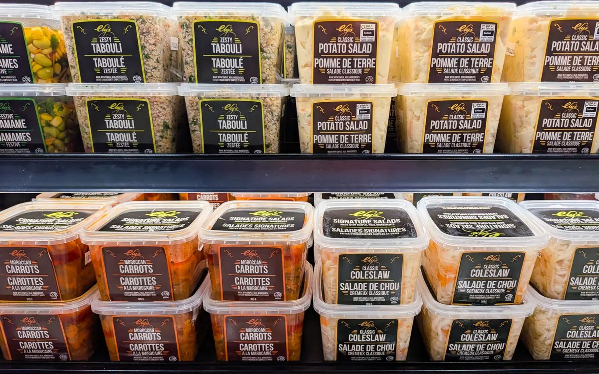 Cooler shelf of Ely's salads in the new labels: Zesty Tabouli in black and lime, Classic Potato Salad in brown and gold, Moroccan Carrots in maroon and orange, and Classic Coleslaw in dark green and gold